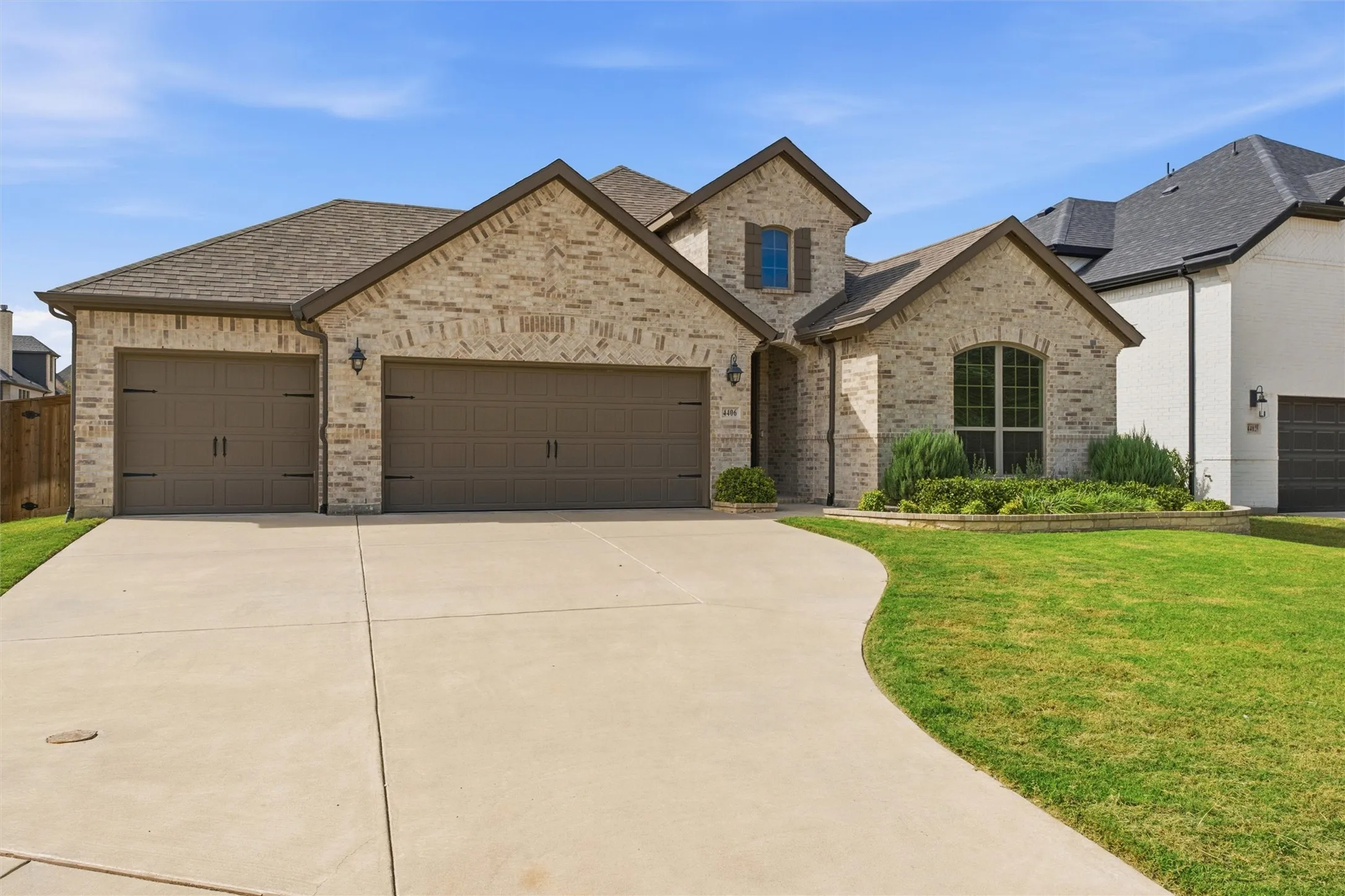 Brick exterior featuring a multi-gabled roofline, three-car garage with carriage-style hardware, arched window detailing, and manicured landscaping