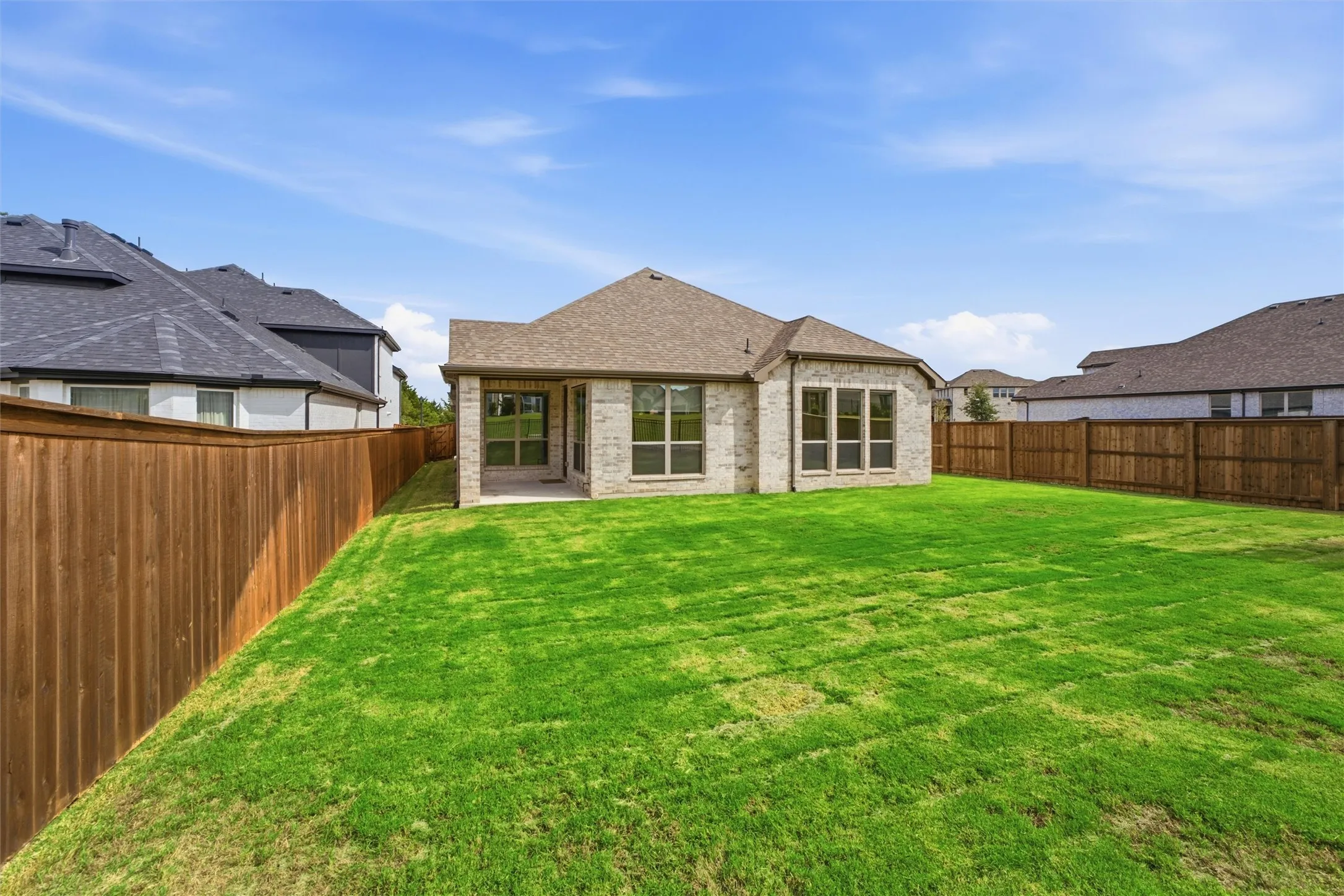 Exterior featuring a light-colored masonry facade, covered rear patio, expansive grass lawn, and full-perimeter wood fencing