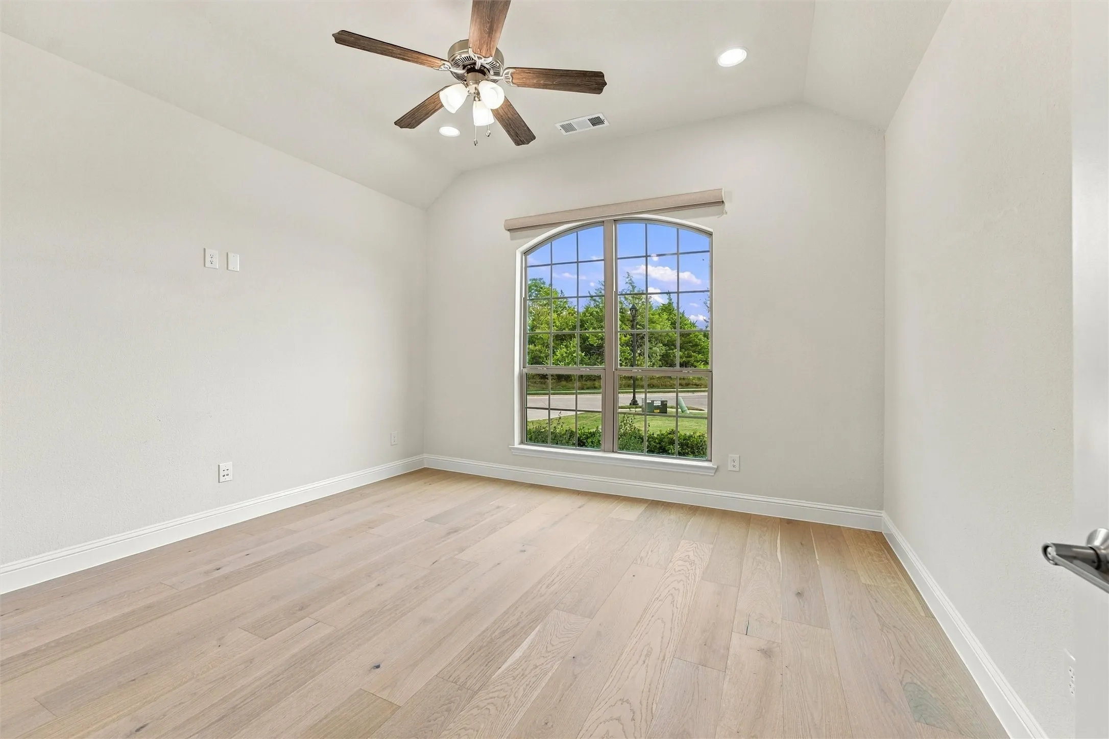 Vaulted ceilings featuring a central fan with integrated lighting, wood-finish flooring, and an arched window