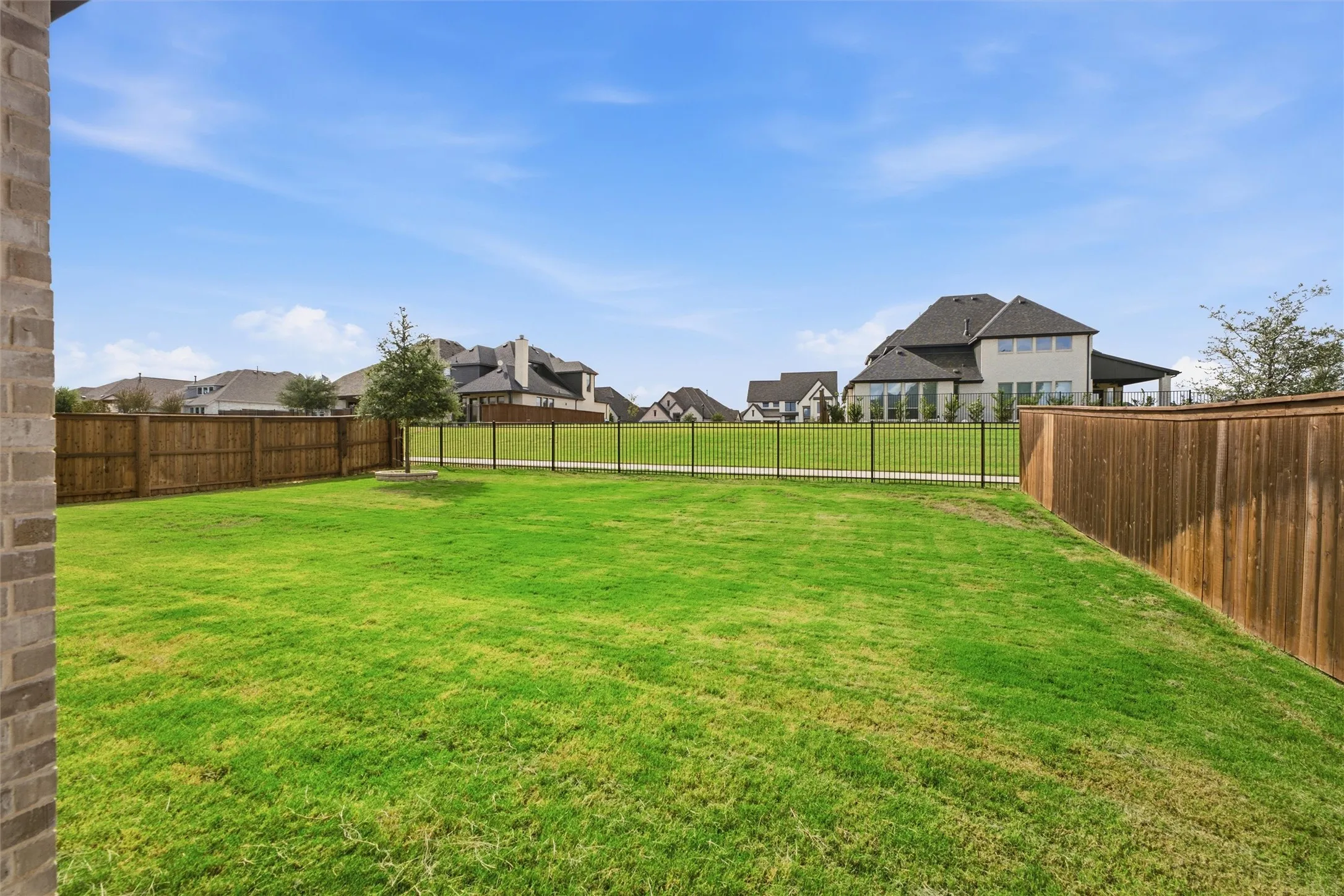 Expansive backyard featuring a manicured lawn, wood privacy fencing, and metal perimeter fencing
