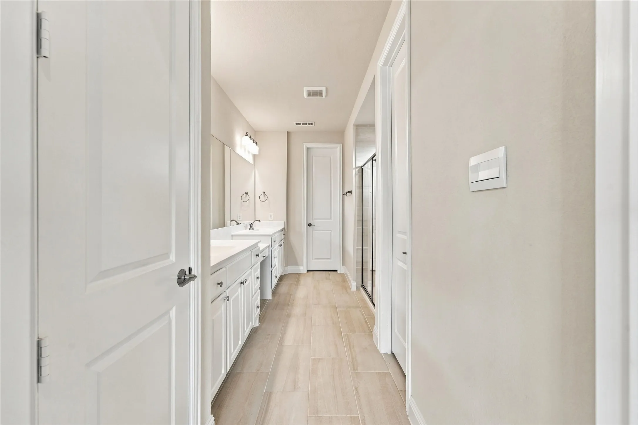 White cabinetry with solid surface countertops, dual sinks, large wall-mounted mirror, and ceramic tile flooring