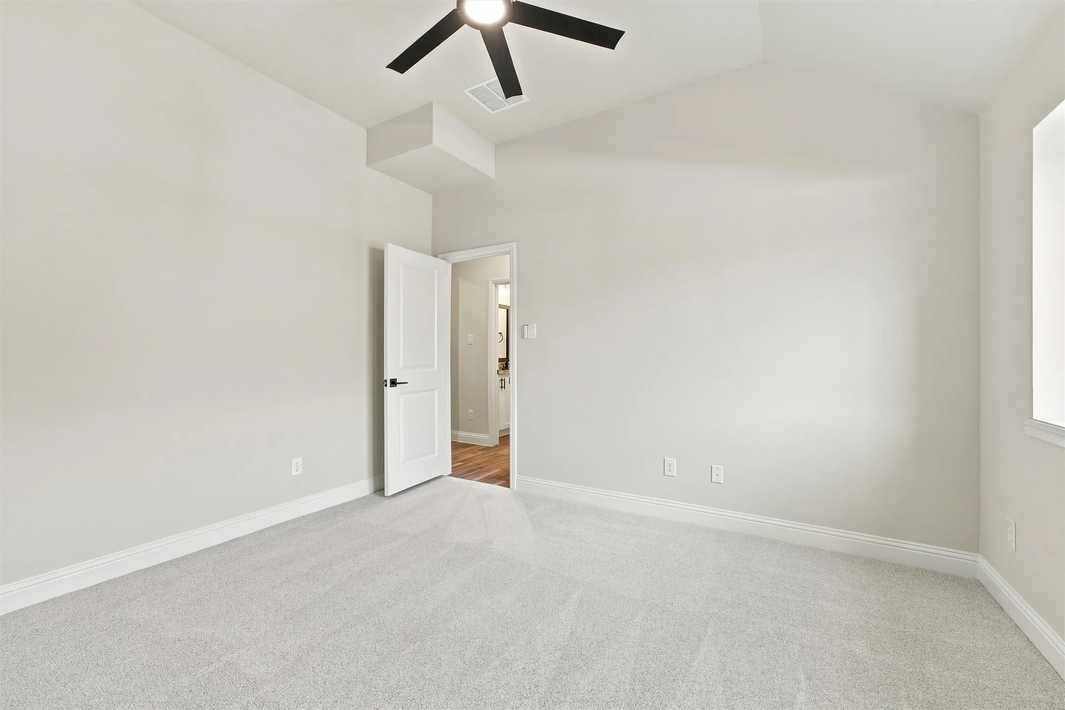 Vaulted ceiling featuring a central matte black ceiling fan with an integrated light fixture, neutral wall palette, and wall-to-wall carpeting