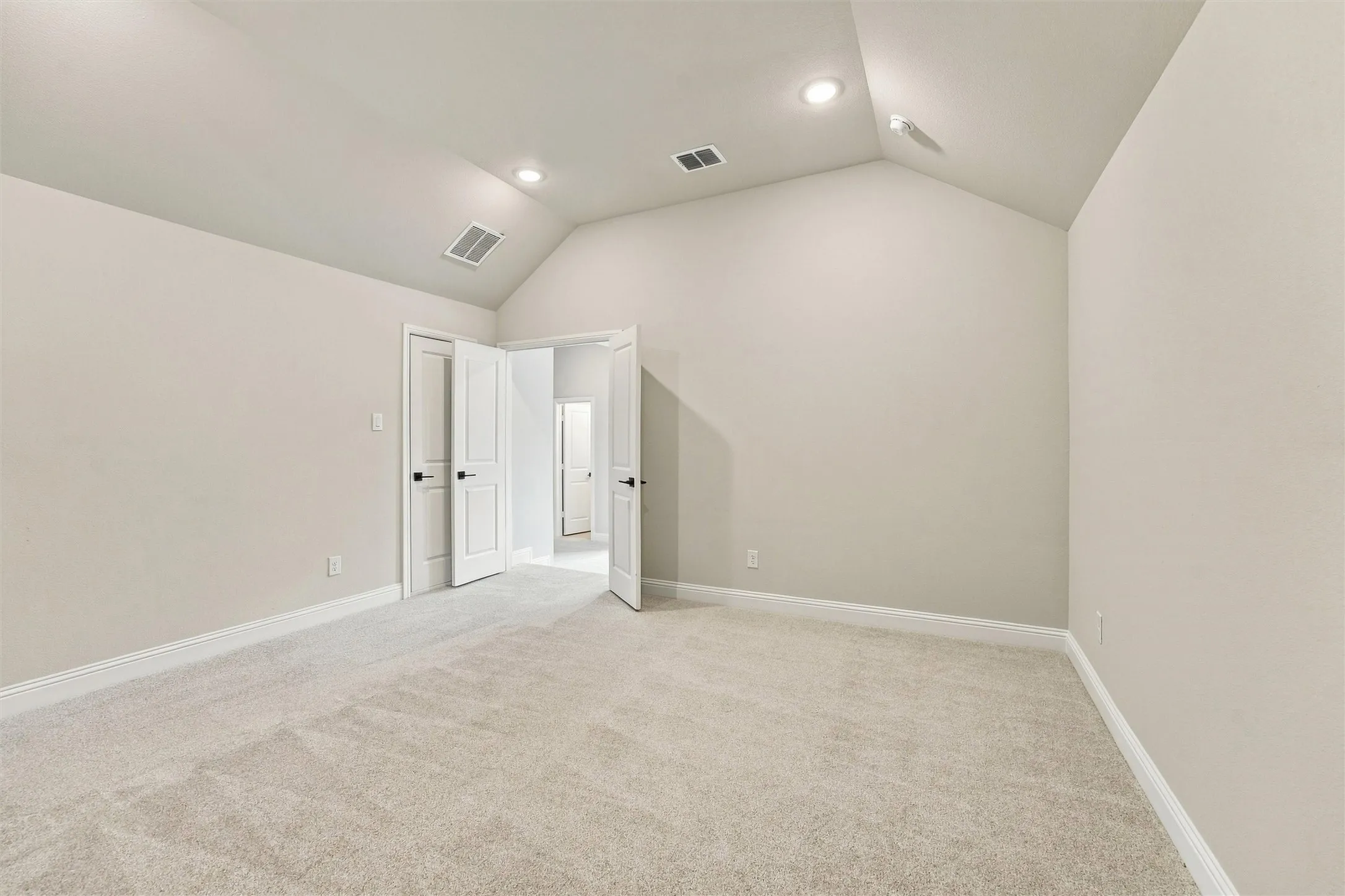 Vaulted ceiling featuring recessed lighting and neutral wall finishes, complemented by wall-to-wall carpeting and paneled interior doors with matte black hardware