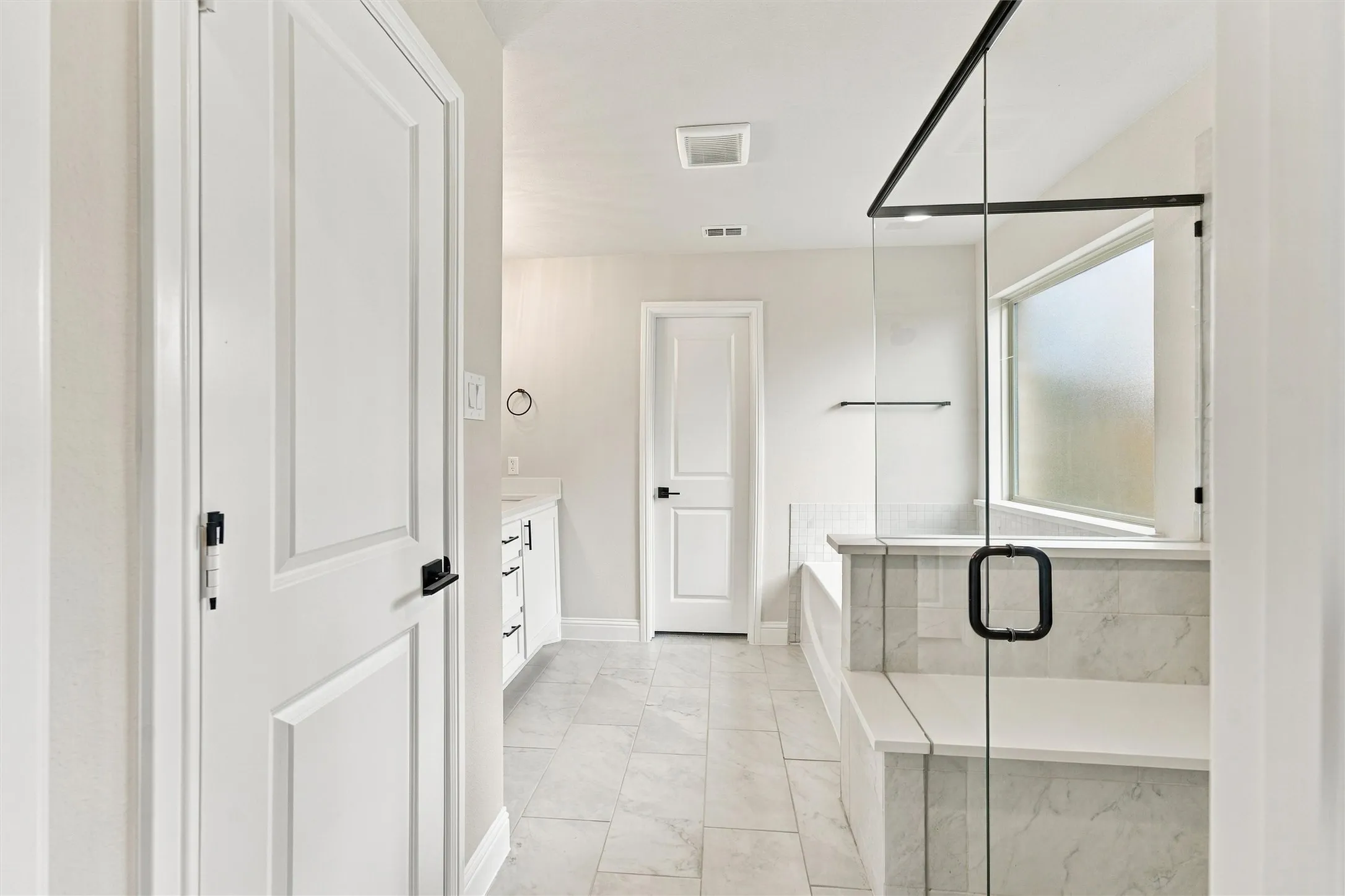 Bathroom featuring a walk-in shower with stone-patterned tile, a glass enclosure with matte black hardware, tile flooring, and white cabinetry