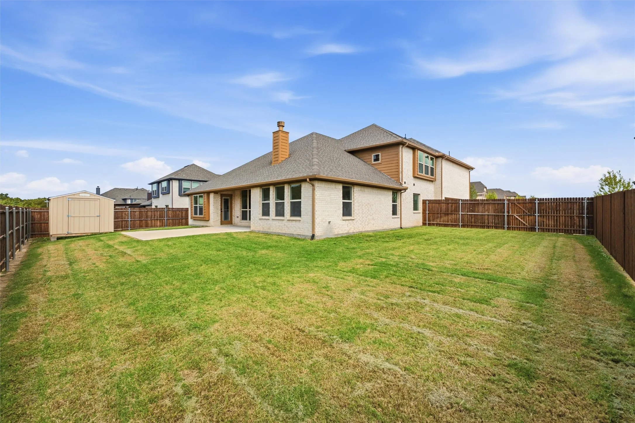 Expansive backyard featuring a sod lawn, concrete patio, perimeter wood fencing, and a detached storage shed