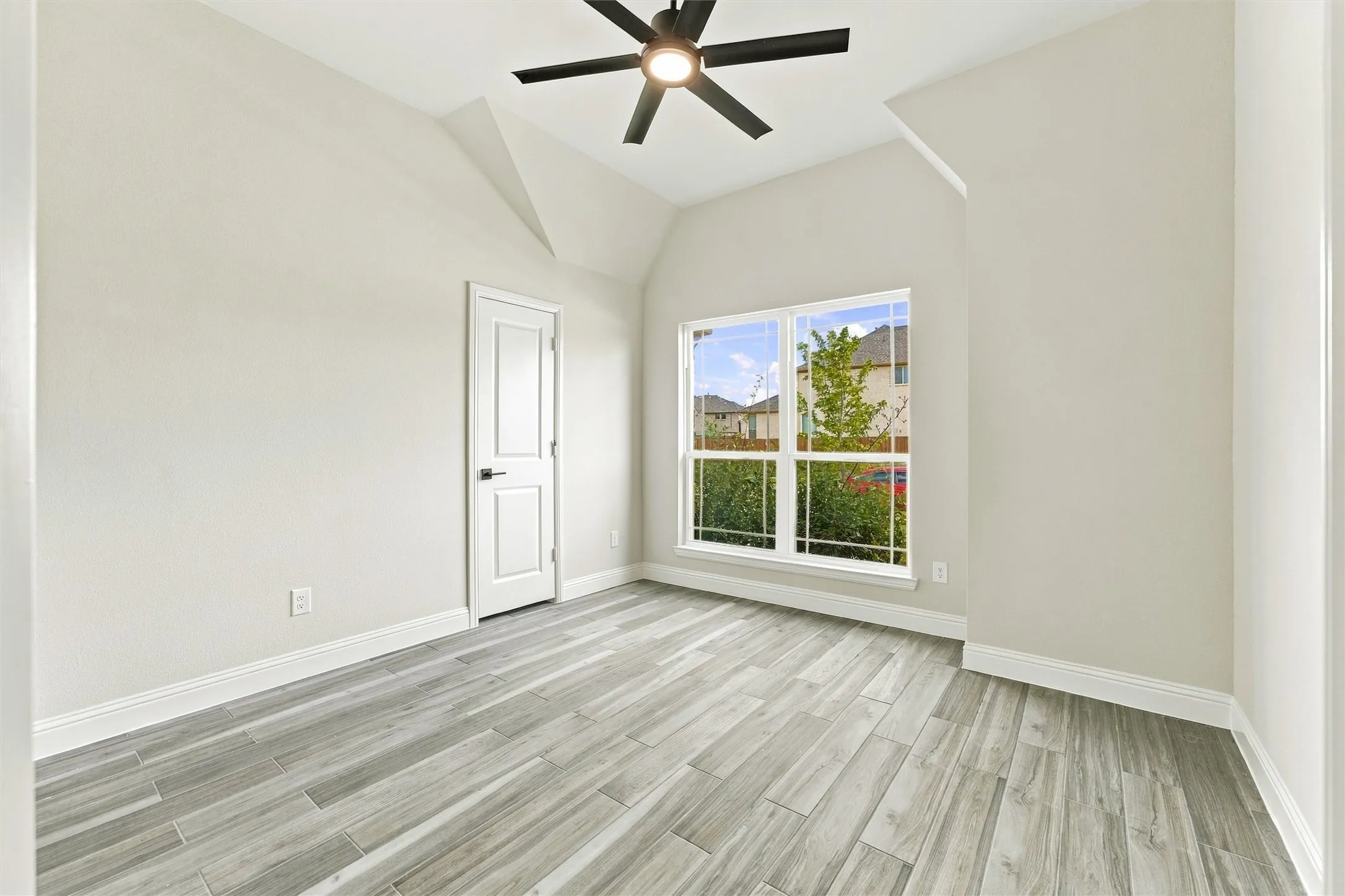 Vaulted ceiling room featuring wood-finish tile flooring, a multi-blade ceiling fan with integrated lighting, and a multi-pane window