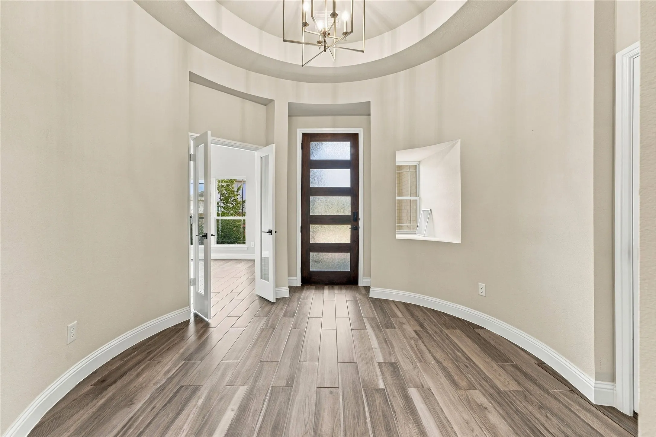 Rotunda foyer featuring a circular tray ceiling, wood-finish flooring, a tiered geometric chandelier, and an entry door with frosted glass panels