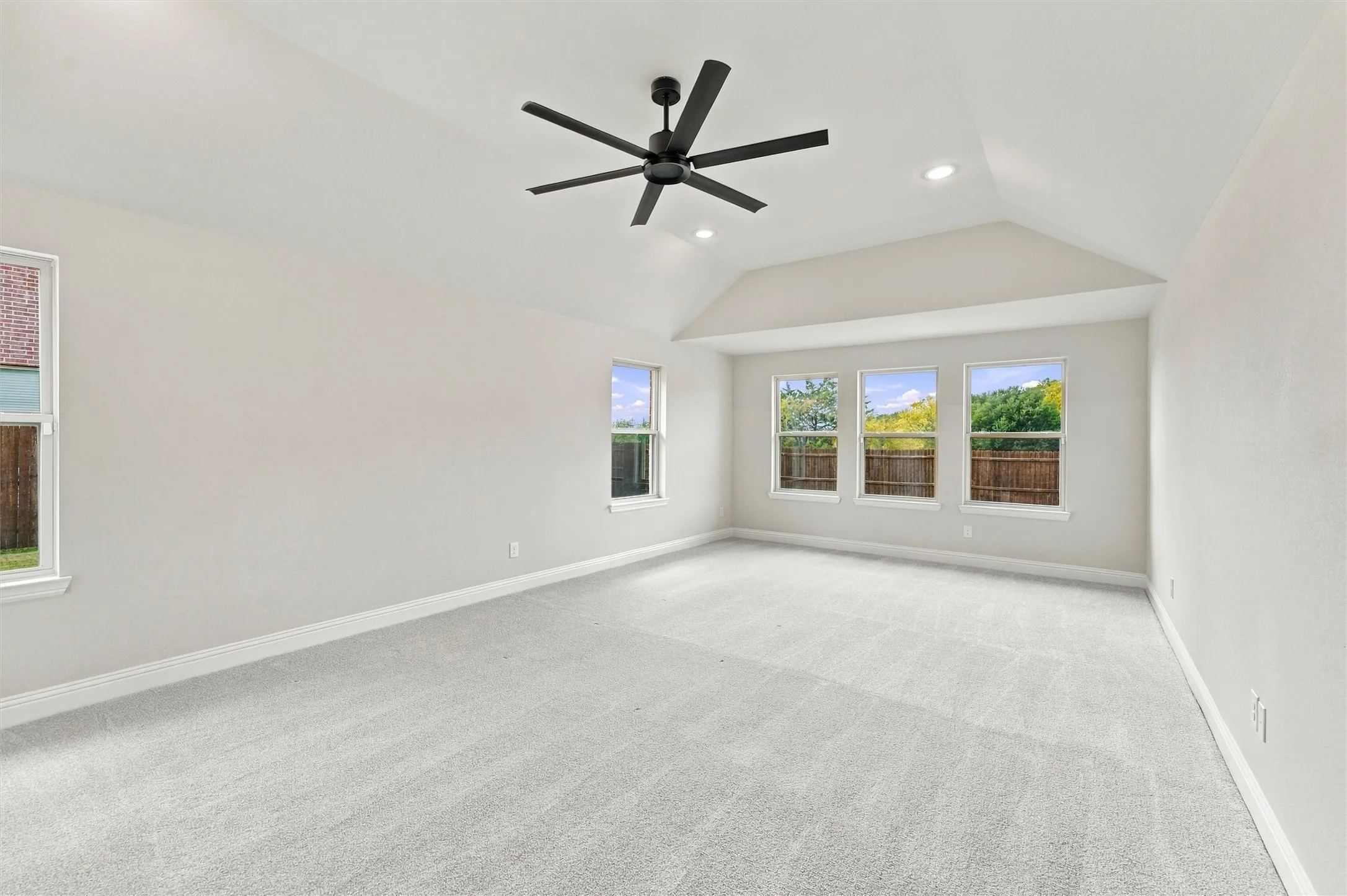 Vaulted ceilings, neutral carpeting, matte black multi-blade ceiling fan, recessed lighting, and large windows
