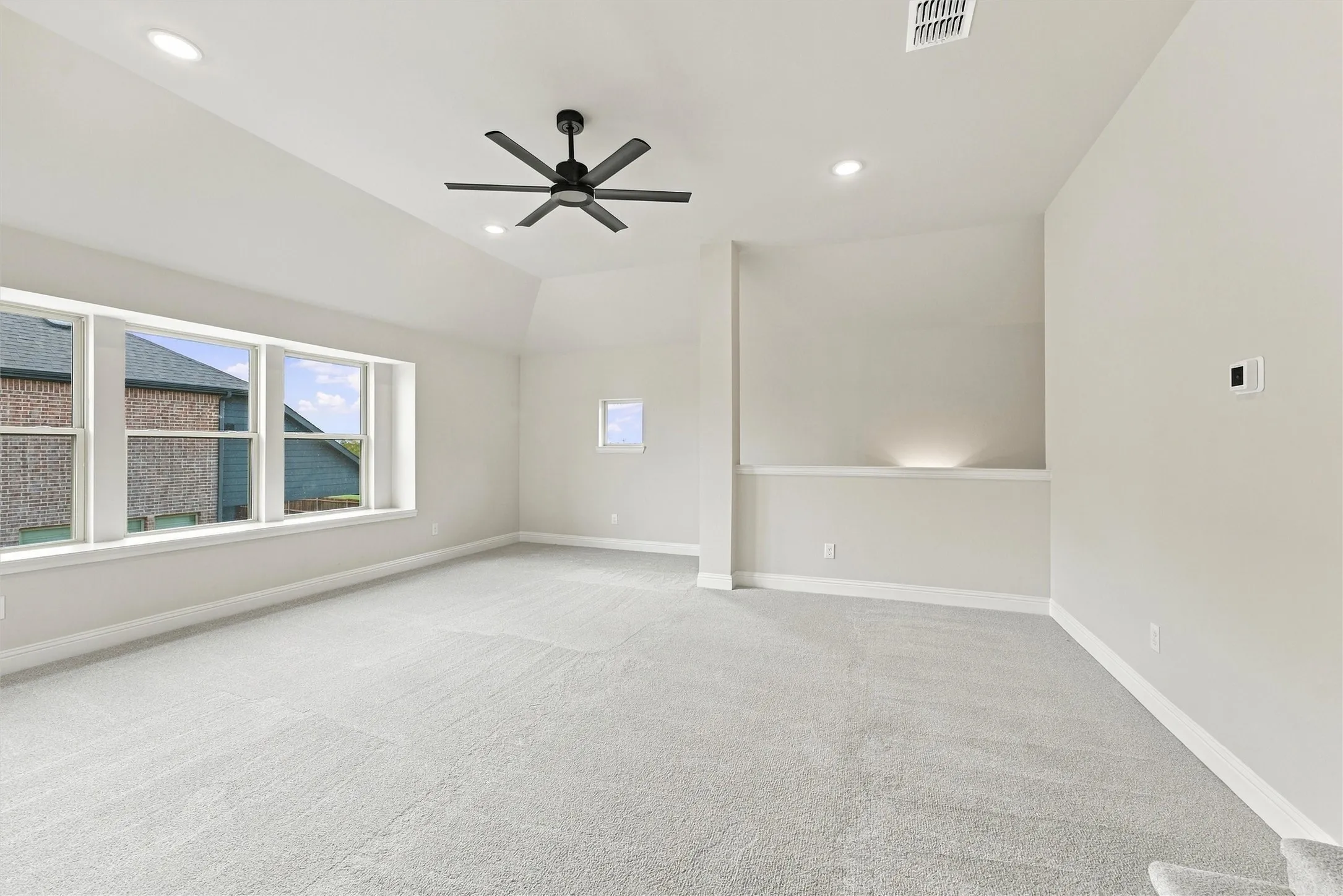 Spacious room featuring a vaulted ceiling, neutral wall-to-wall carpeting, recessed lighting, and a multi-blade ceiling fan