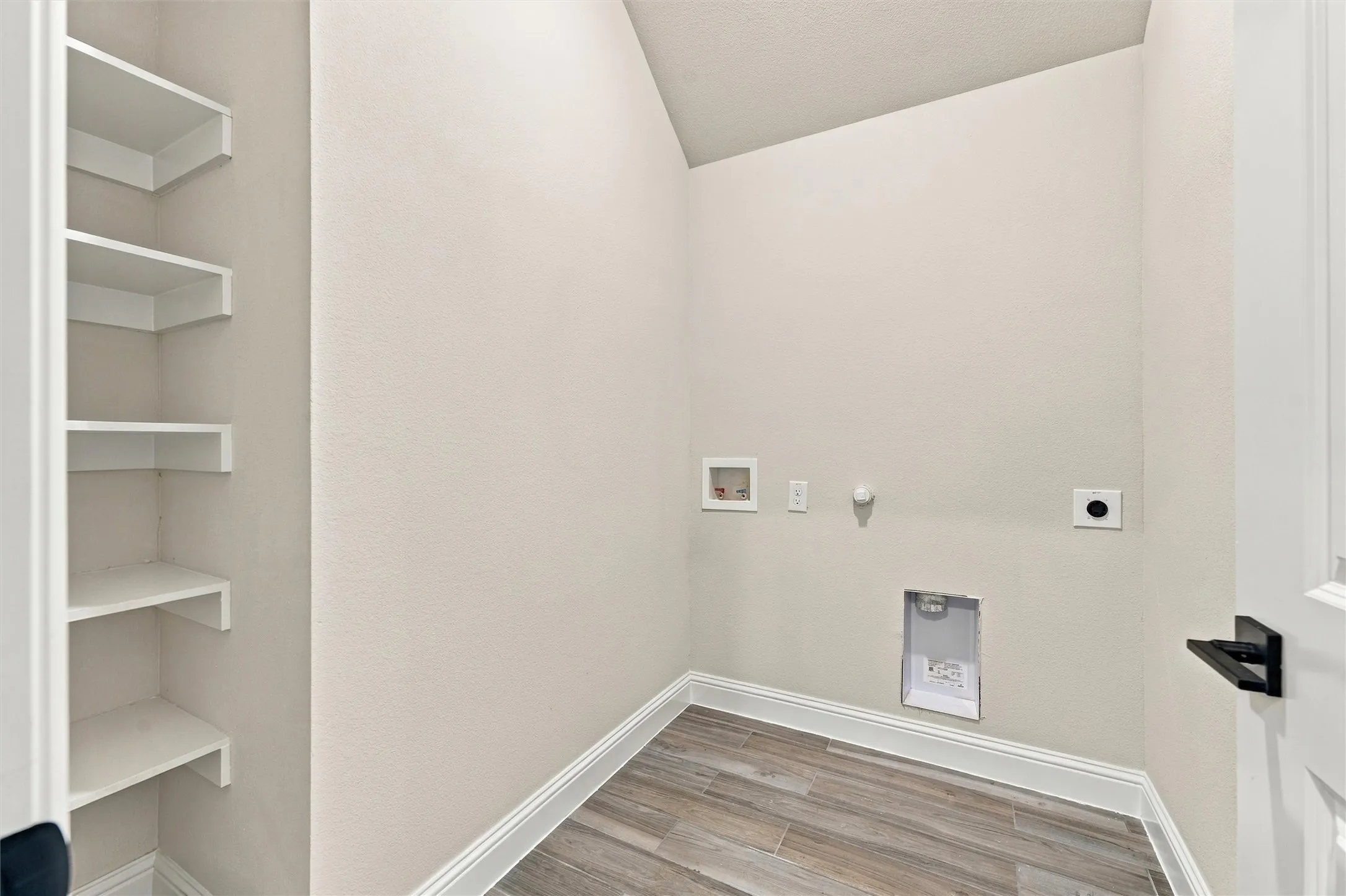 Utility space featuring built-in open shelving, wood-finish flooring, and wall-mounted plumbing and electrical hookups