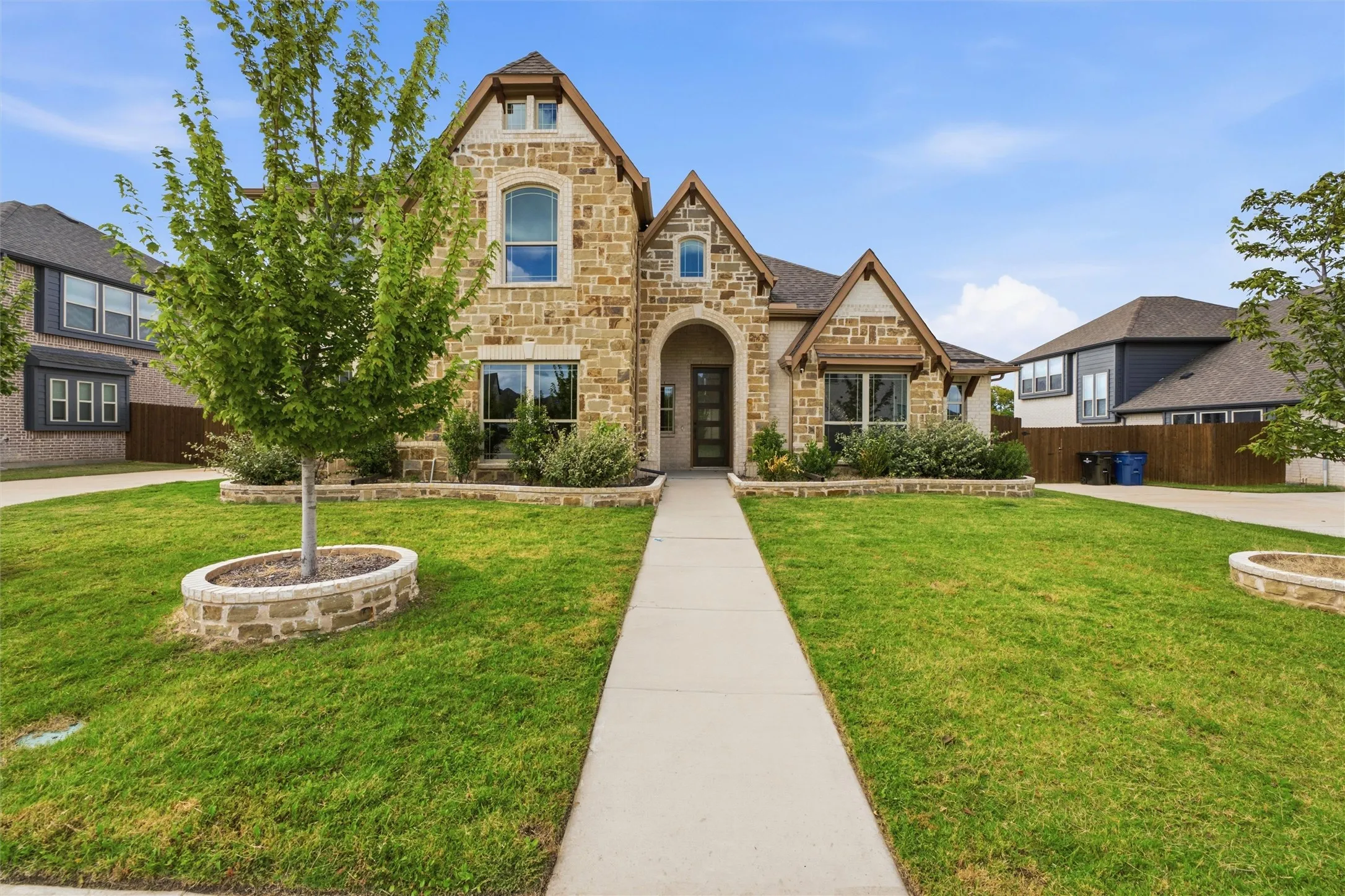 Stone and stucco exterior featuring a gabled roofline, arched entryway, and stone-bordered landscaping