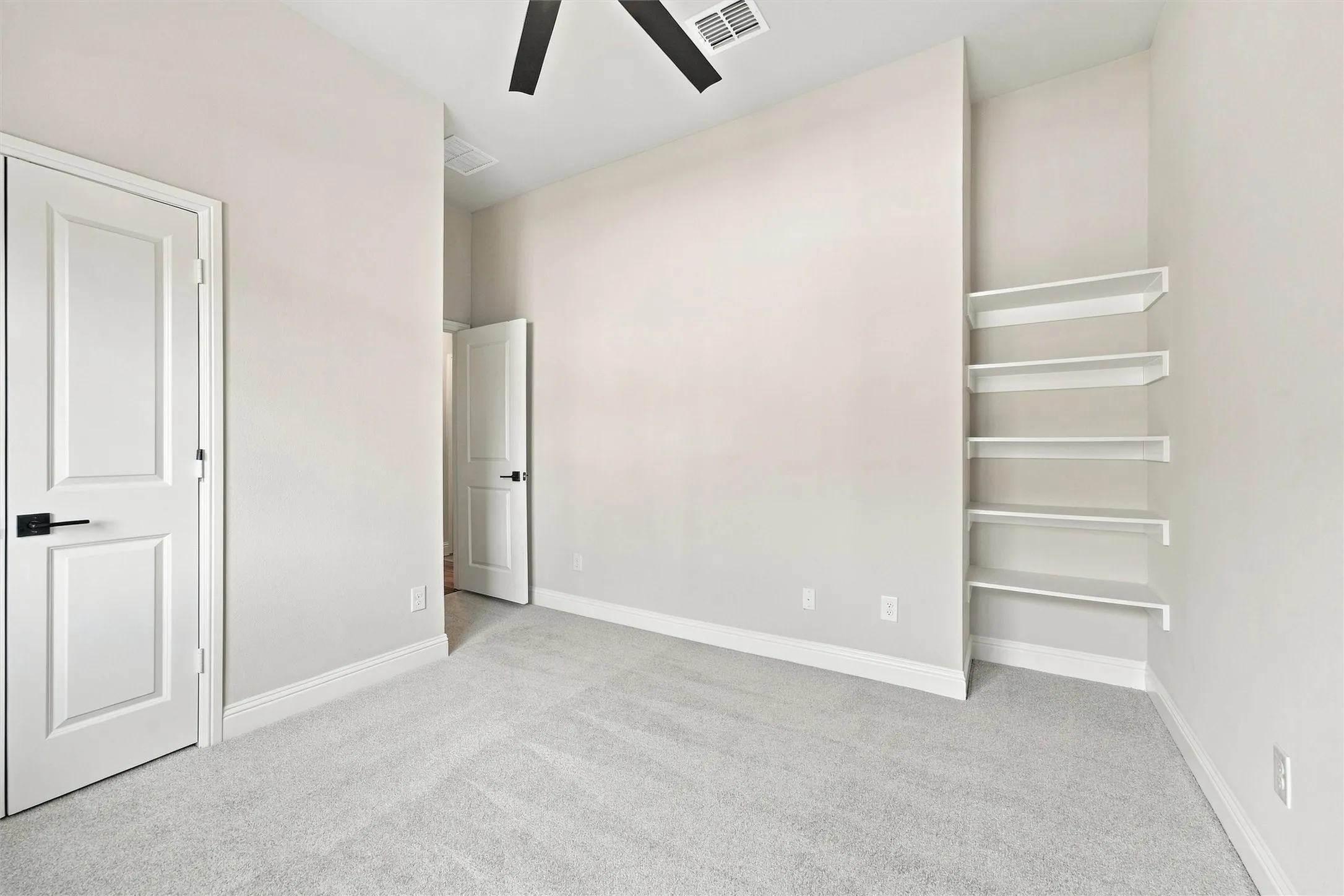Room featuring high ceilings, neutral wall tones, carpeted flooring, built-in shelving, and a ceiling fan