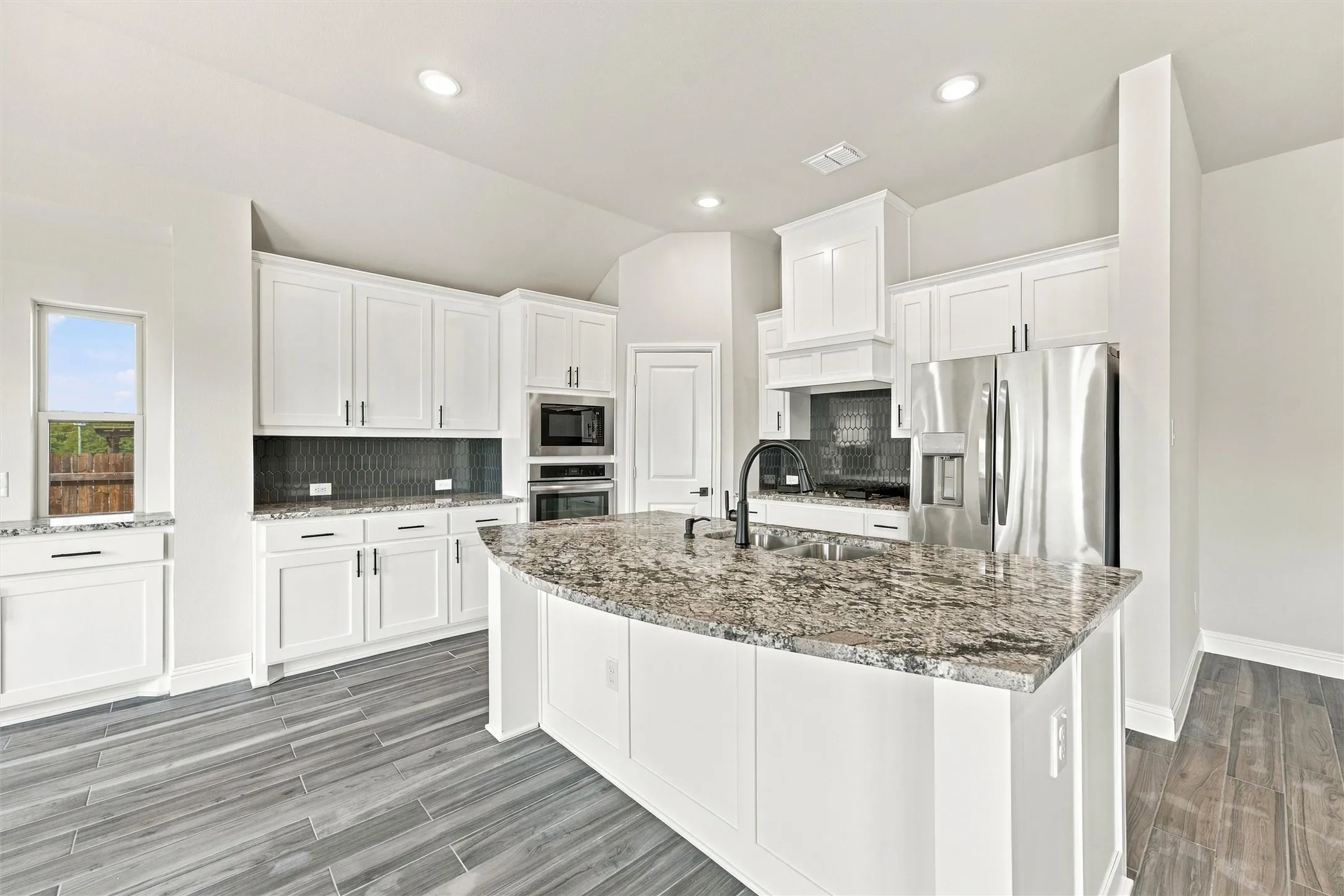 Kitchen featuring white cabinetry, an expansive central island with stone-finish countertops, dark tile backsplash, stainless steel appliances, and wood-finish tile flooring