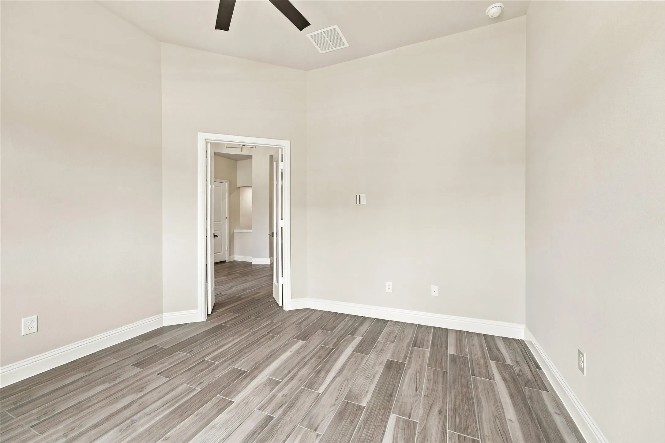 Room with wood-finish flooring, high ceilings, ceiling fan, and double-door entry