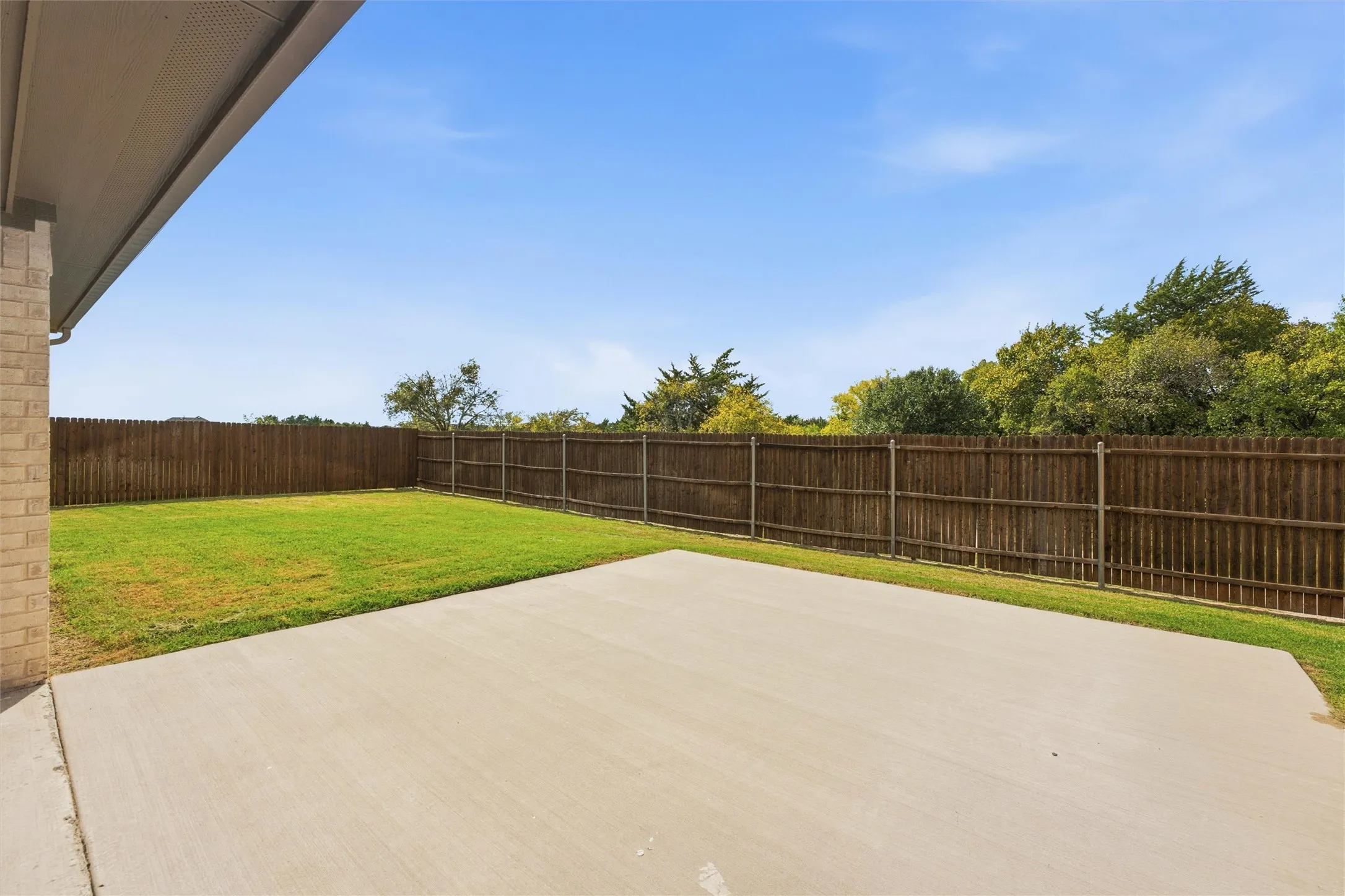 Rear exterior space featuring a concrete patio, grass lawn, and wood privacy fencing
