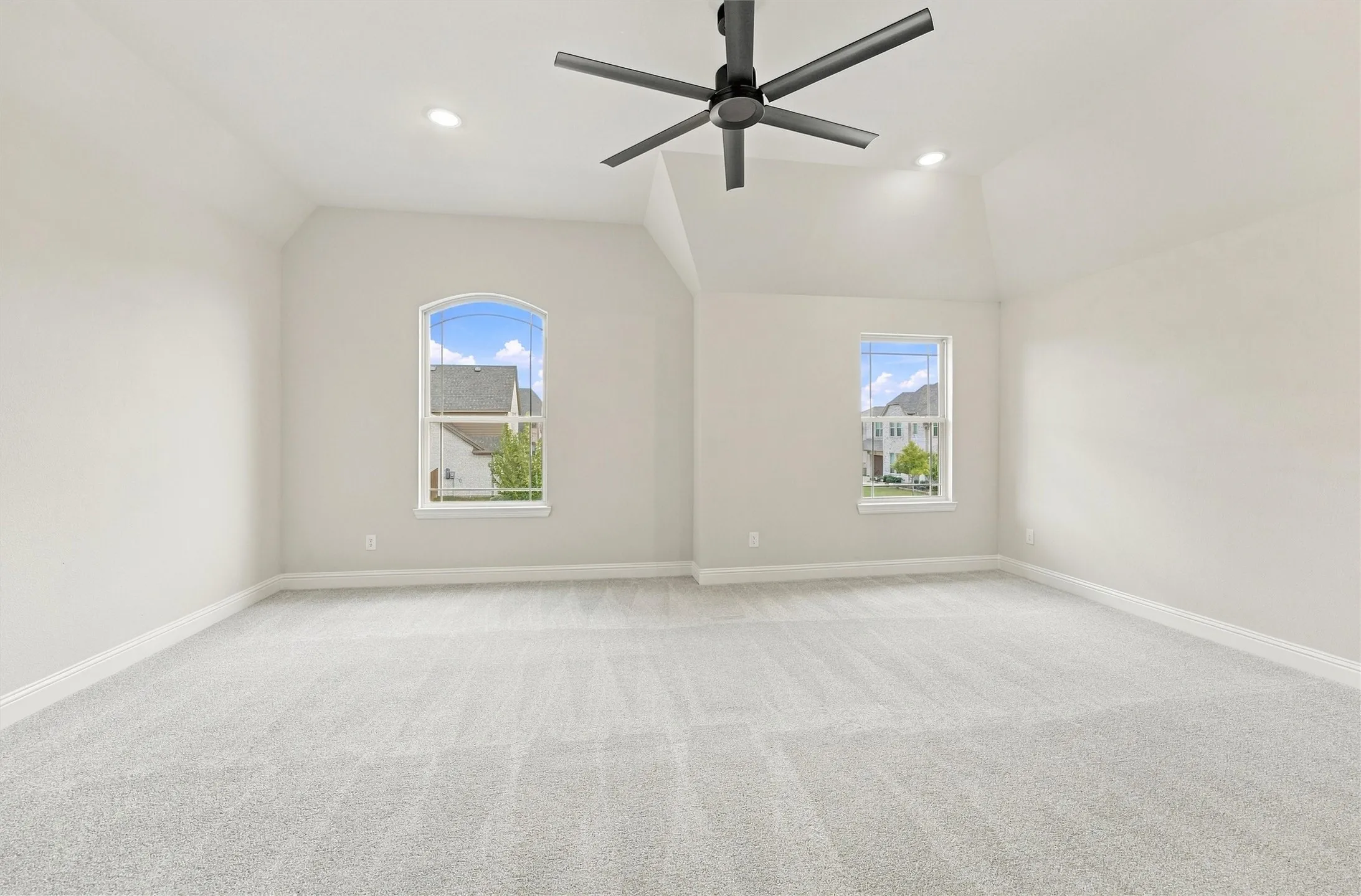 Vaulted ceilings featuring recessed lighting, a multi-blade ceiling fan, and large windows including one arched design with carpeted flooring