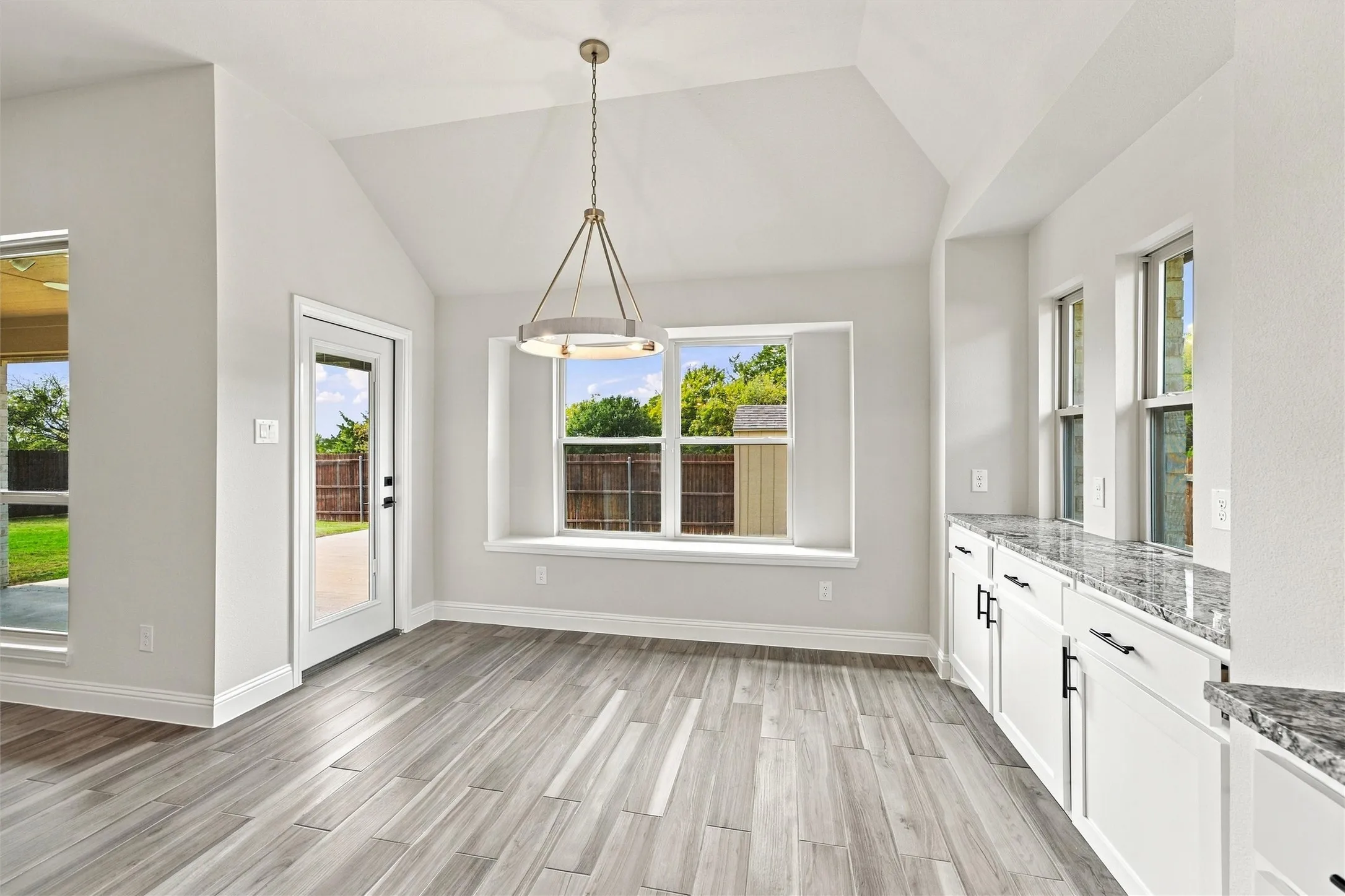 Vaulted ceiling space featuring wood-finish flooring, built-in cabinetry with stone-finish countertops, a multi-pane bay window with a ledge, and a circular chandelier