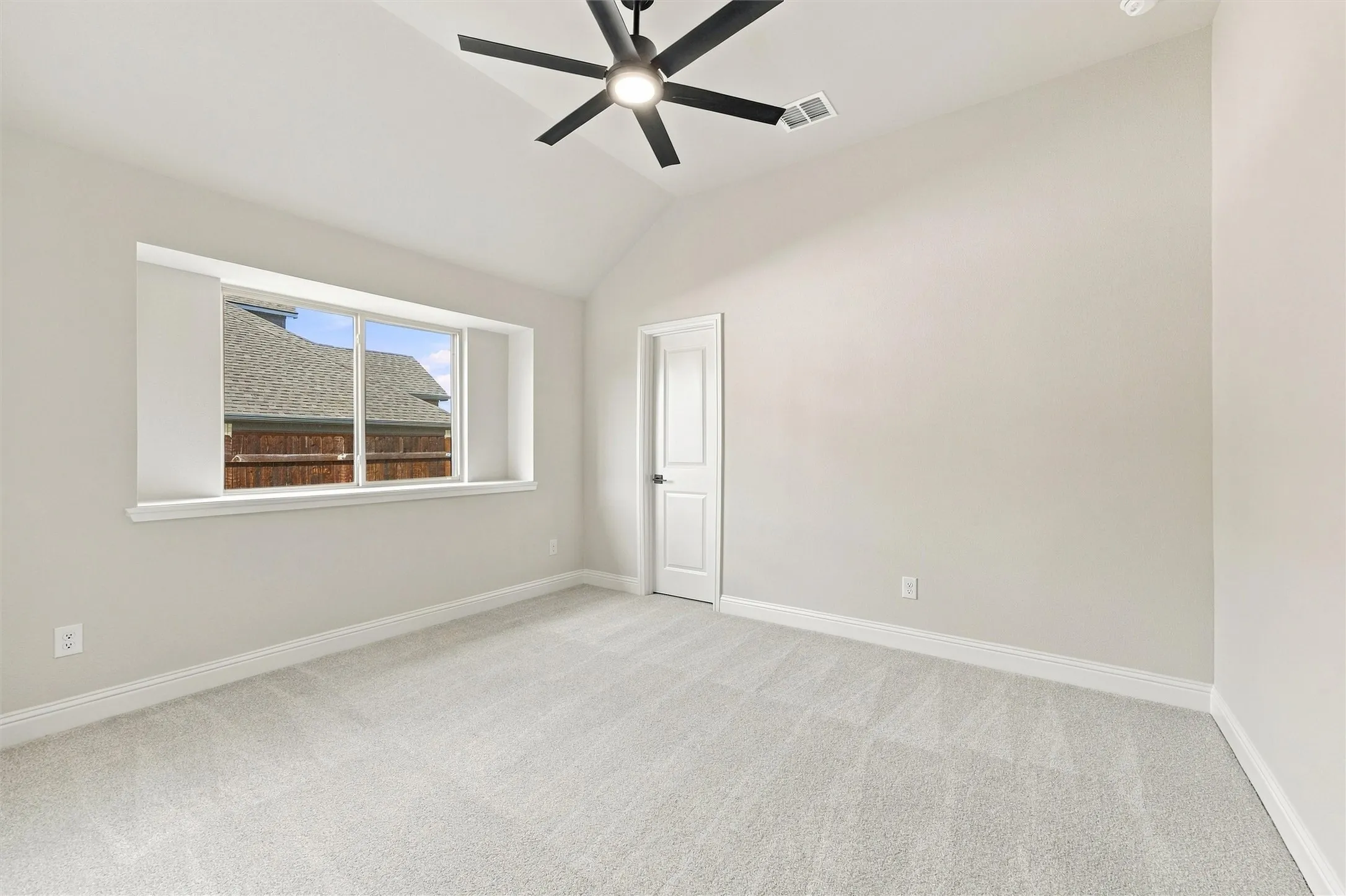 Vaulted ceilings, large picture window, neutral carpeting, and a modern ceiling fan with integrated lighting