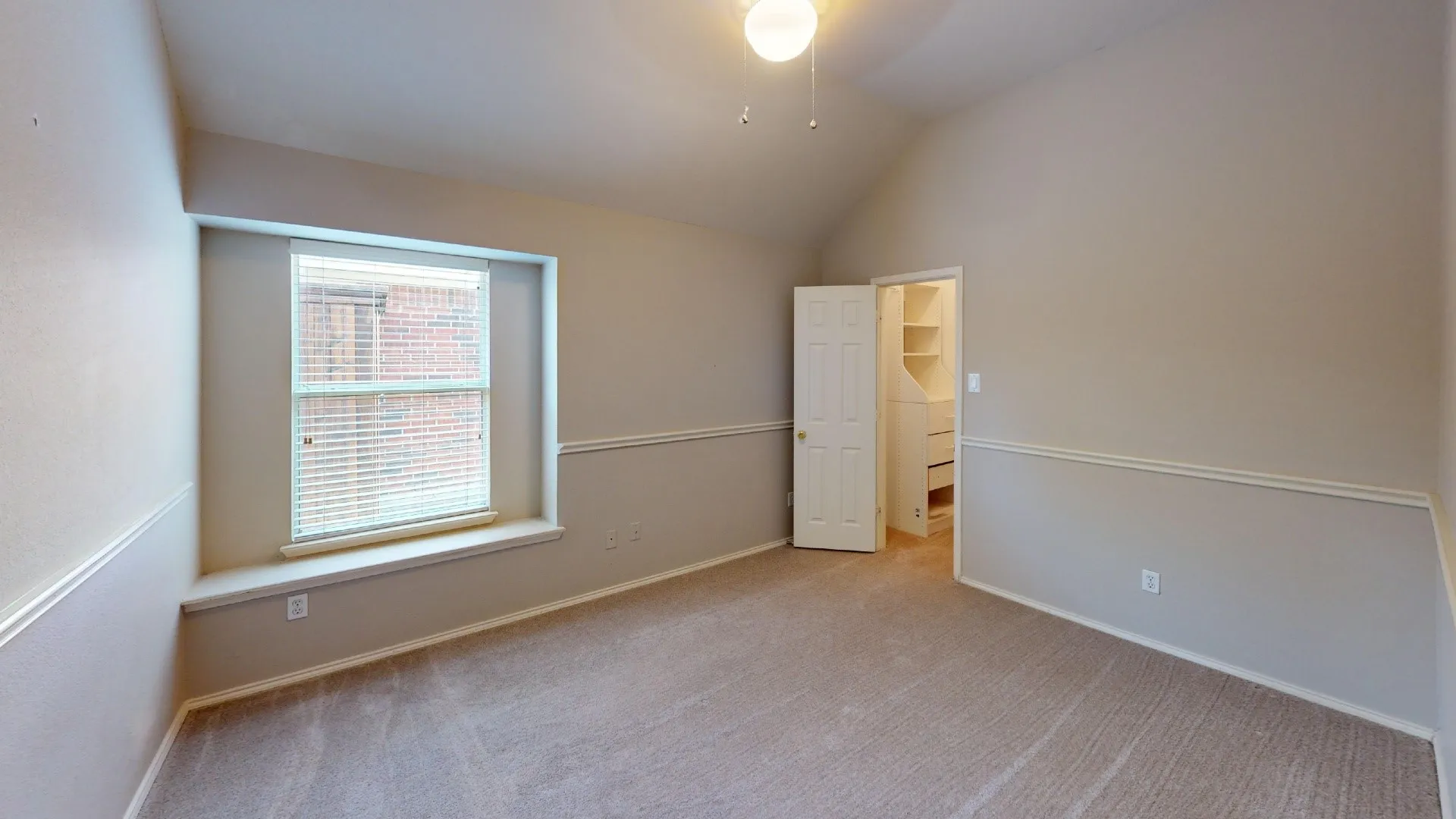 Vaulted ceiling, bay window with built-in ledge, chair rail molding, carpeted flooring, and walk-in storage area