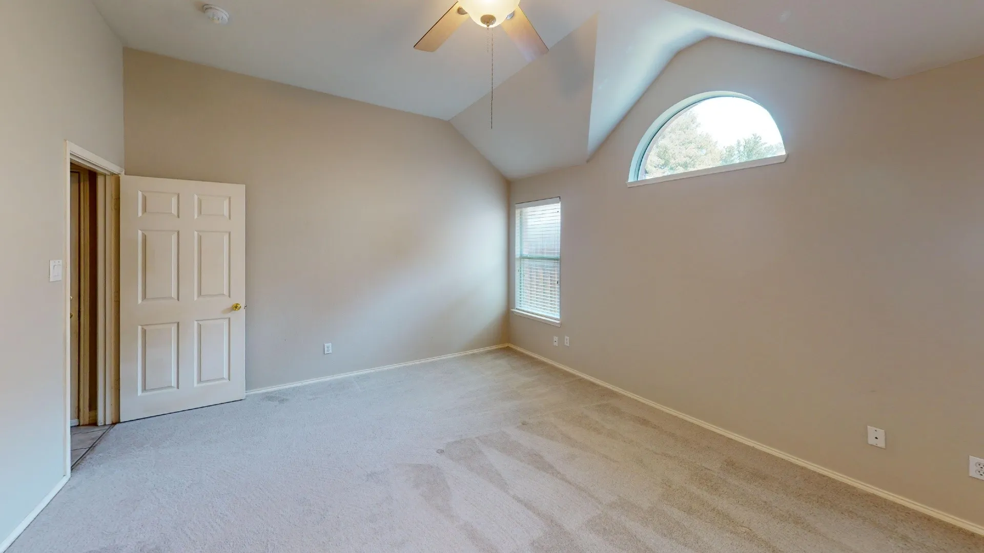 Vaulted ceilings, arched transom window, wall-to-wall carpeting, and a ceiling fan with light fixture