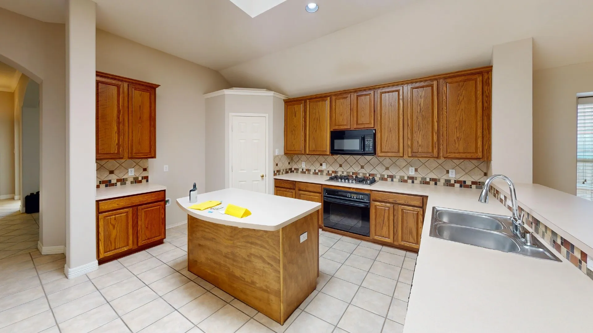 Kitchen featuring wood cabinetry, solid-surface countertops, tile backsplash, center island, and double-basin stainless steel sink
