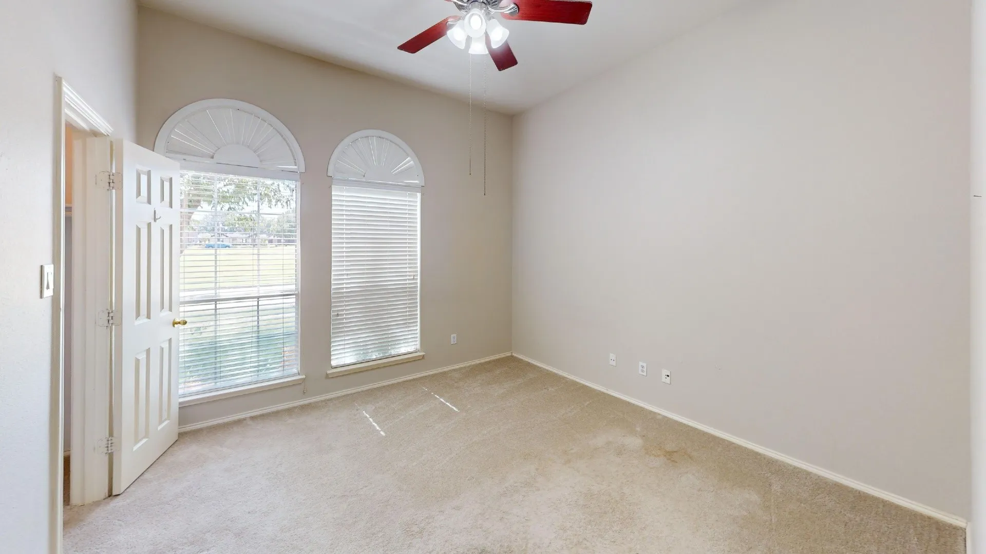 Room featuring high ceilings, two windows with arched transoms, wall-to-wall carpeting, and a ceiling fan with light fixture