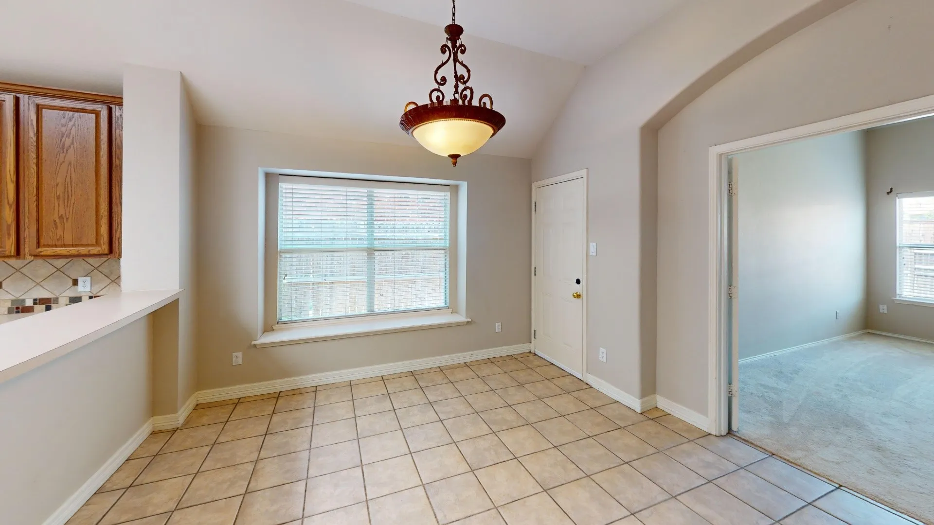 Vaulted ceilings, tile flooring, built-in window seat, ornate hanging light fixture, and arched doorway entry
