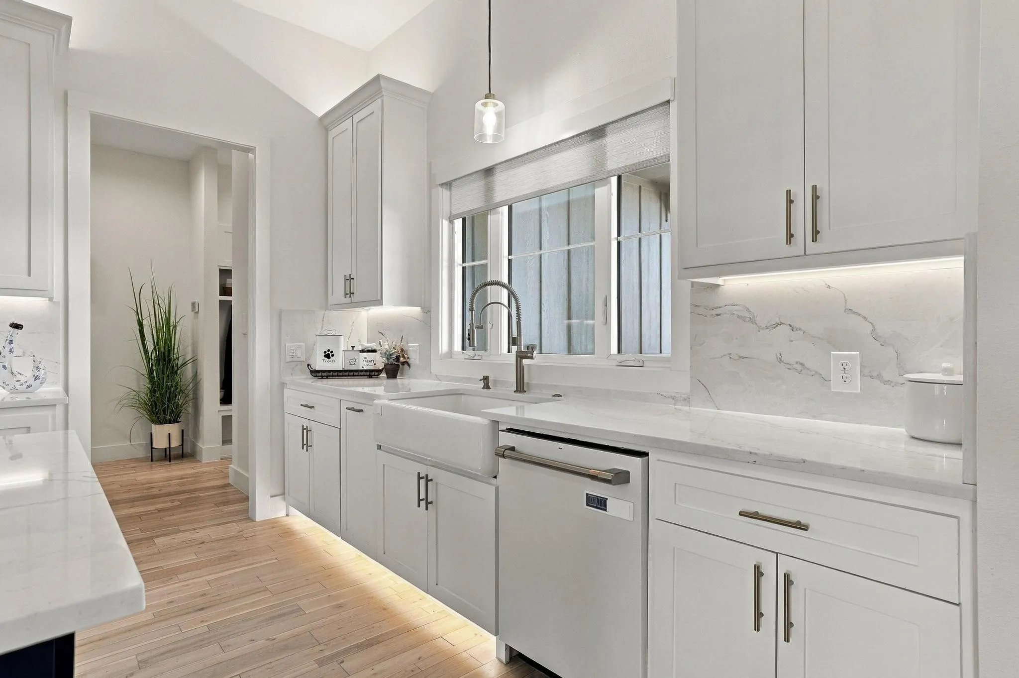 Kitchen featuring shaker-style cabinetry, white countertops with matching backsplash, apron-front sink, under-cabinet lighting, and wood-finish flooring