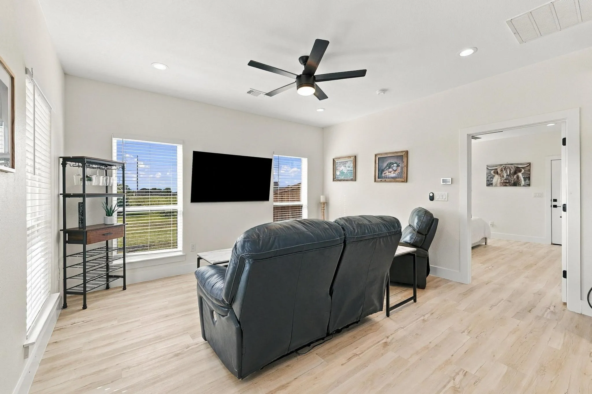 Living area featuring light-toned wood-finish flooring, recessed lighting, a modern ceiling fan, and large windows with integrated blinds