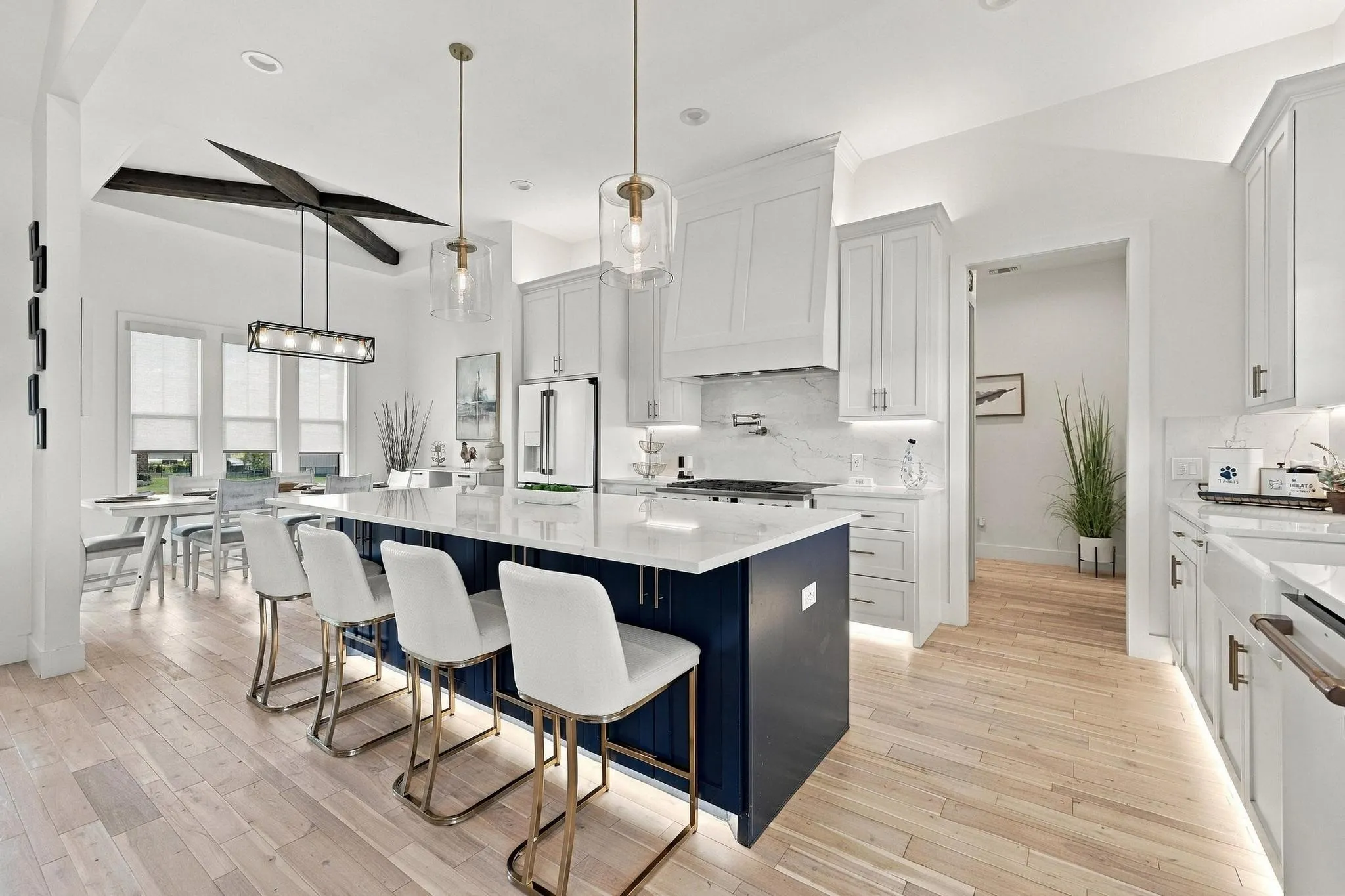 Kitchen featuring a large contrasting navy-blue center island with quartz countertops, custom white cabinetry, wood-finish flooring, and industrial-style pendant lighting