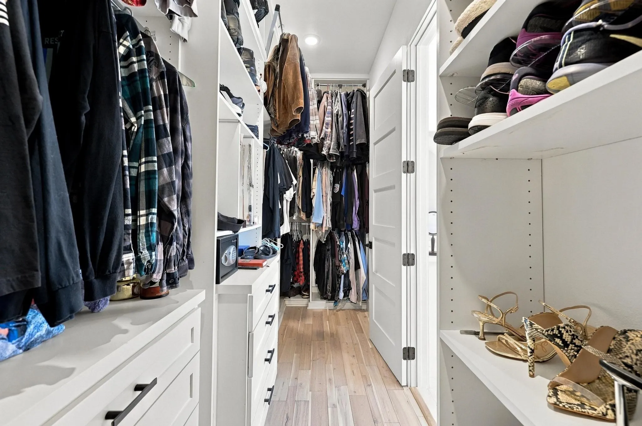 Walk-in closet featuring white custom built-in cabinetry, integrated drawer storage, adjustable shelving, recessed ceiling lighting, and wood-finish flooring