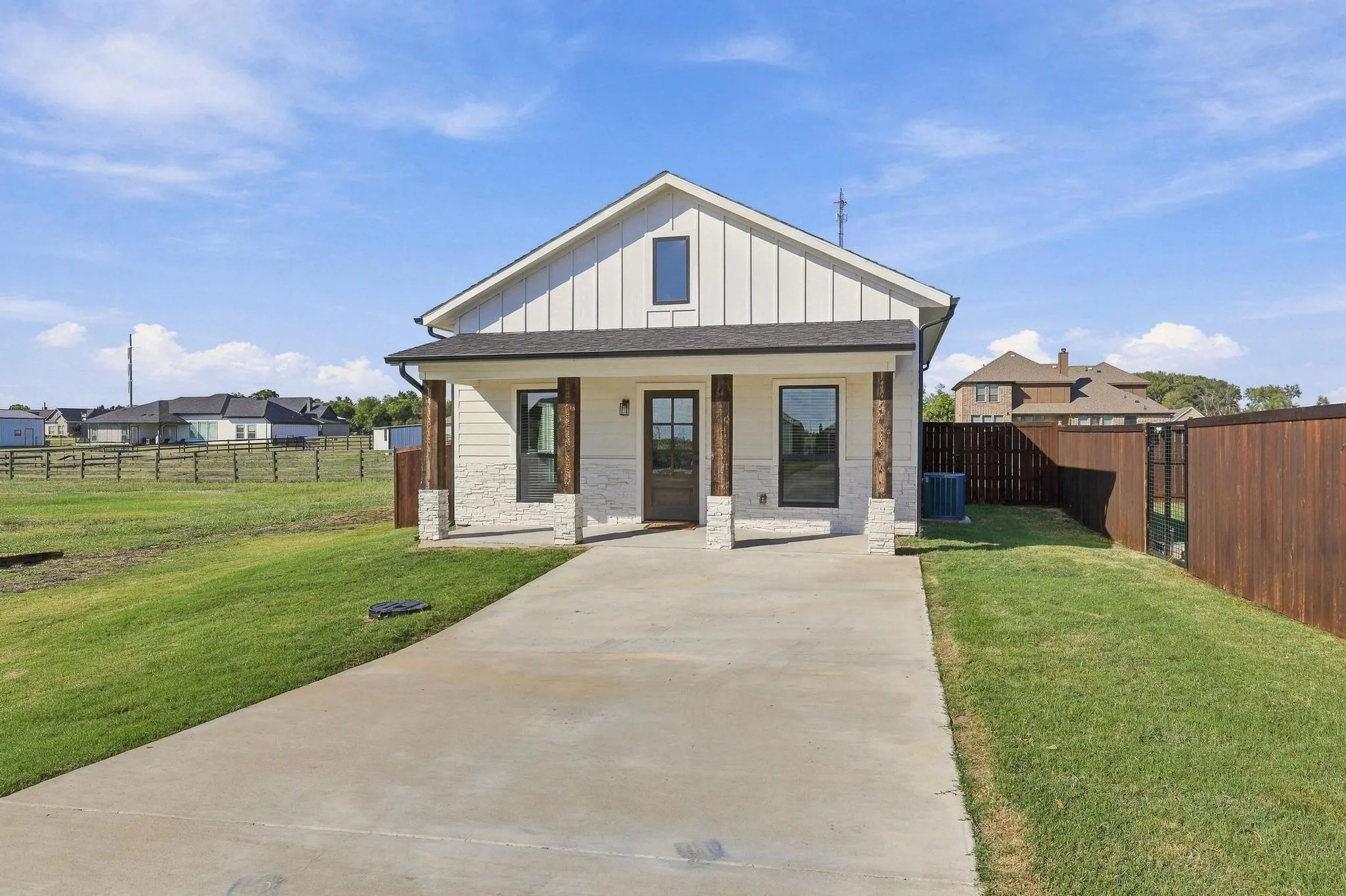 Exterior featuring board-and-batten siding, stone masonry lower facade, wood-finish support columns, a covered porch, and a concrete driveway
