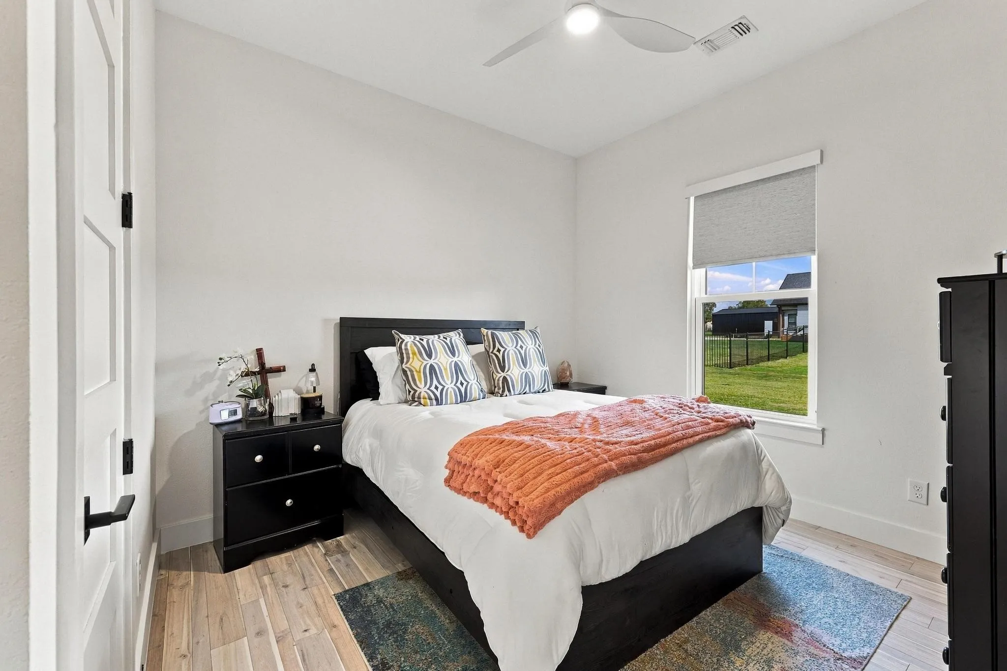 Neutral-toned walls, wood-finish flooring, single-hung window with a roller shade, and a white ceiling fan with integrated lighting