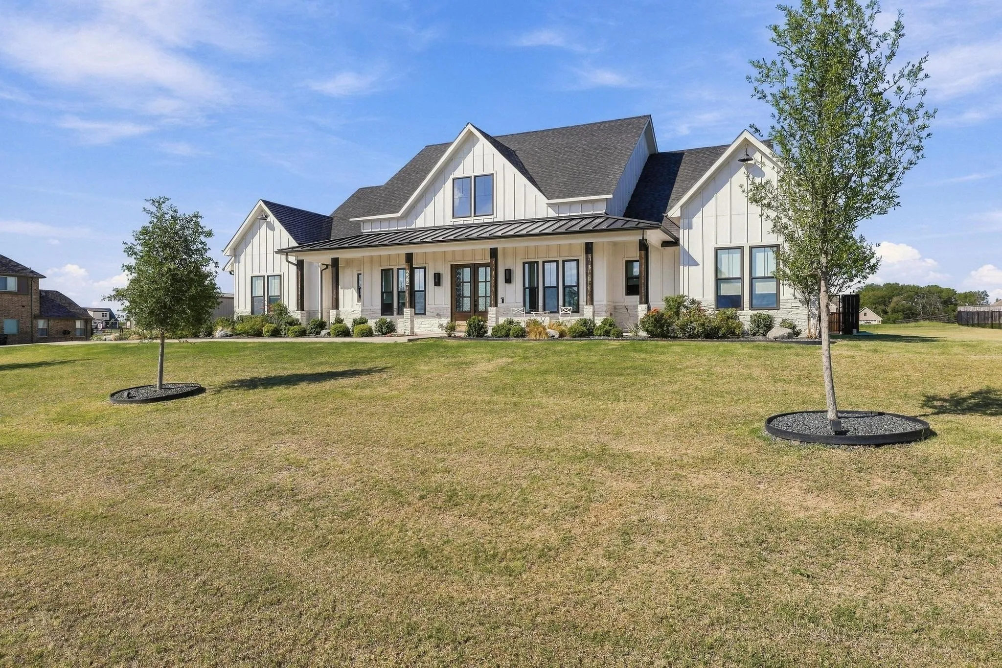 Modern farmhouse exterior featuring vertical board-and-batten siding, stone accents, a covered front porch with metal roofing, and multiple multi-pane windows