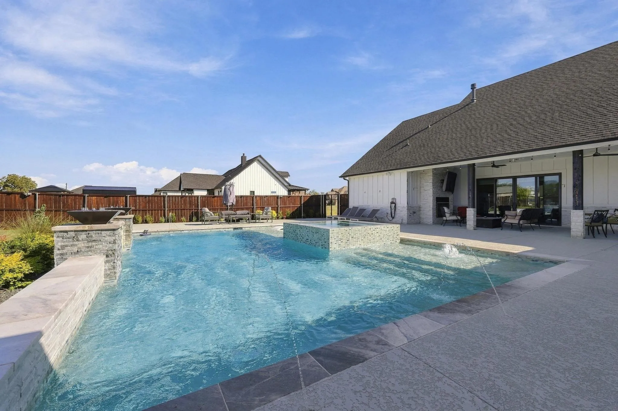 Backyard oasis featuring a swimming pool with a raised spa, stone-veneer fire features, a covered patio with a built-in outdoor fireplace, and concrete decking