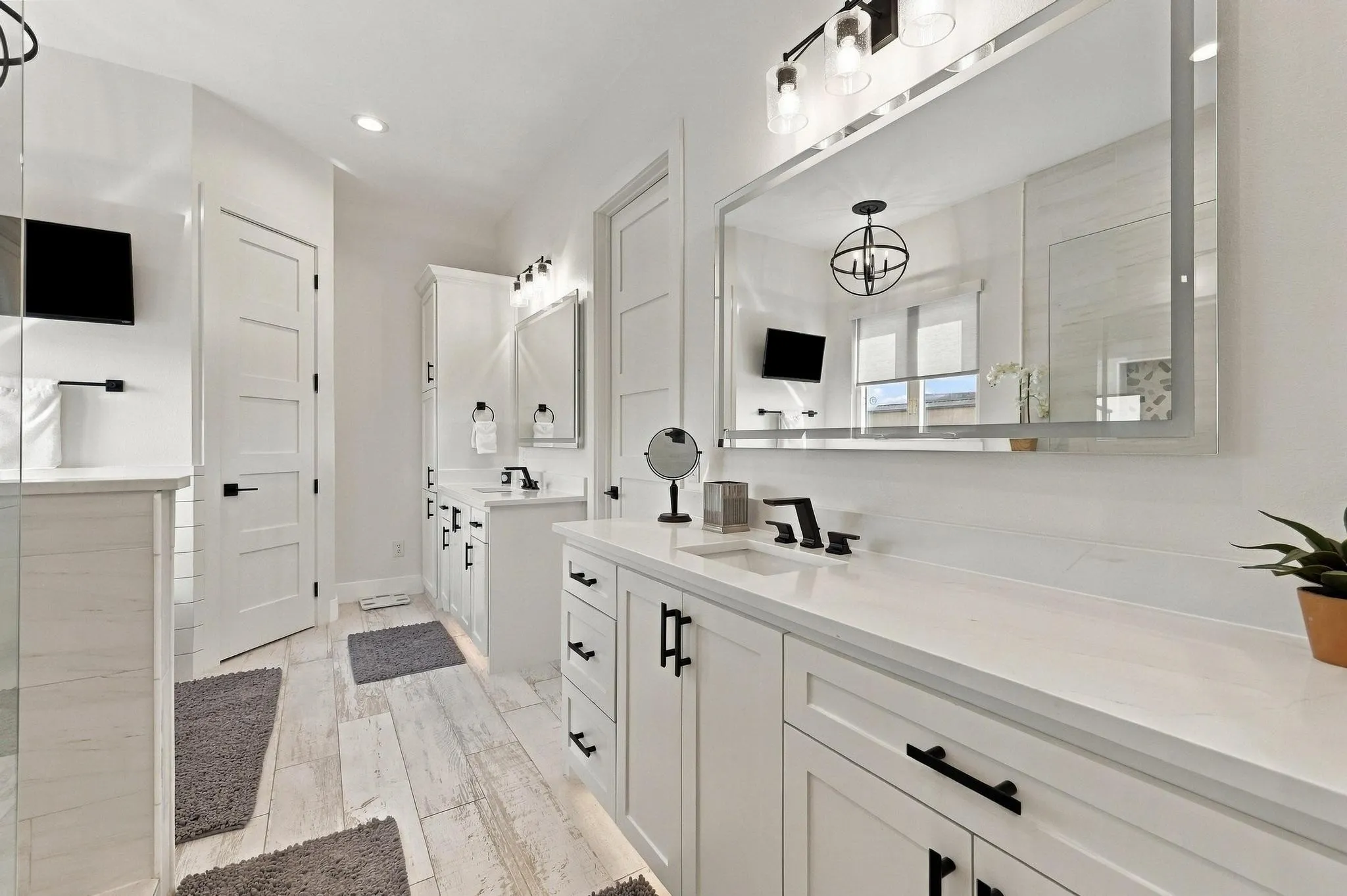 Dual-vanity bathroom featuring white cabinetry, light-toned stone-finish countertops, matte black hardware, large-format framed mirrors, and wood-finish tile flooring