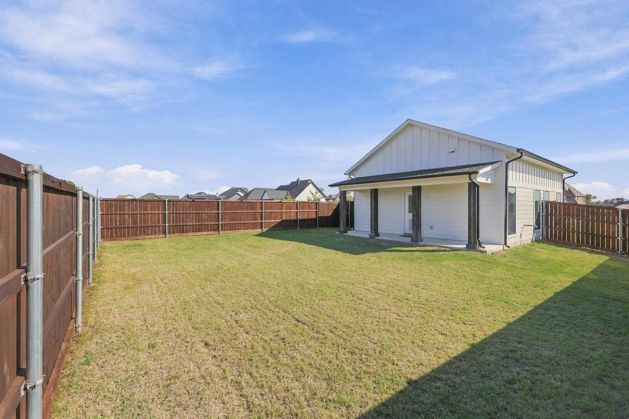 Expansive backyard featuring a level lawn, full-height wood privacy fencing, and a covered rear patio with structural columns