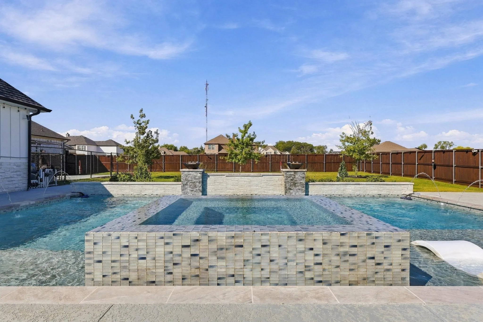 In-ground swimming pool featuring a central raised spa with tile surround, stone-accented water feature, tanning ledge, and perimeter concrete decking