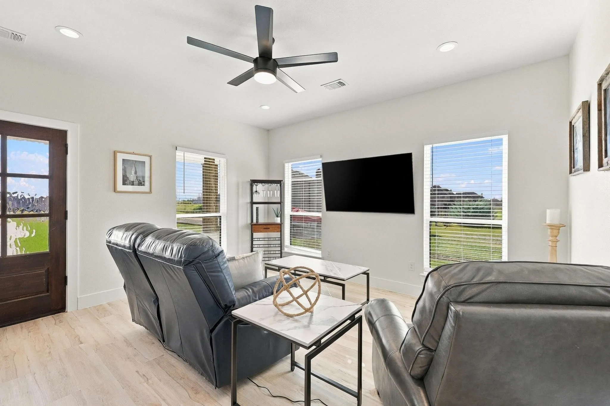 Living area featuring wood-finish flooring, high ceilings with a matte black modern ceiling fan, recessed lighting, and multiple windows with horizontal blinds