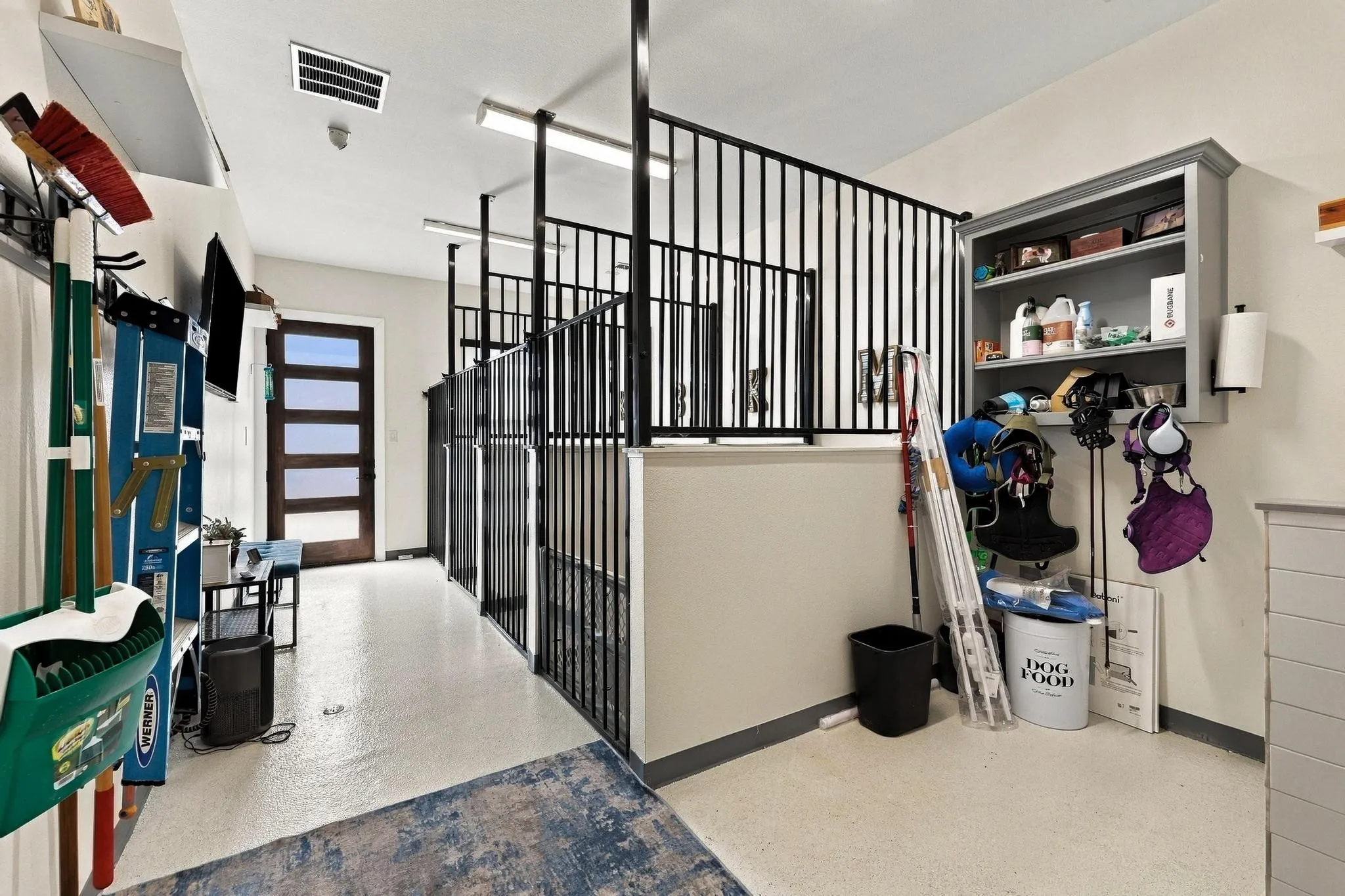 Interior space featuring black metal vertical bar partitions, wall-mounted open shelving, epoxy flooring, and a multi-panel door with glass inserts