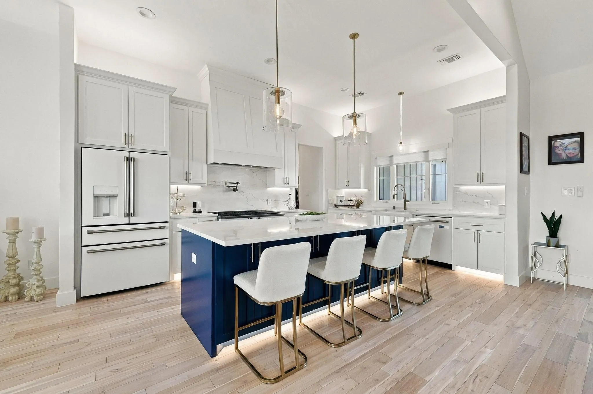 Kitchen featuring a central blue island with white countertops, light-toned wood-finish flooring, white shaker-style cabinetry, a custom range hood, and pendant lighting