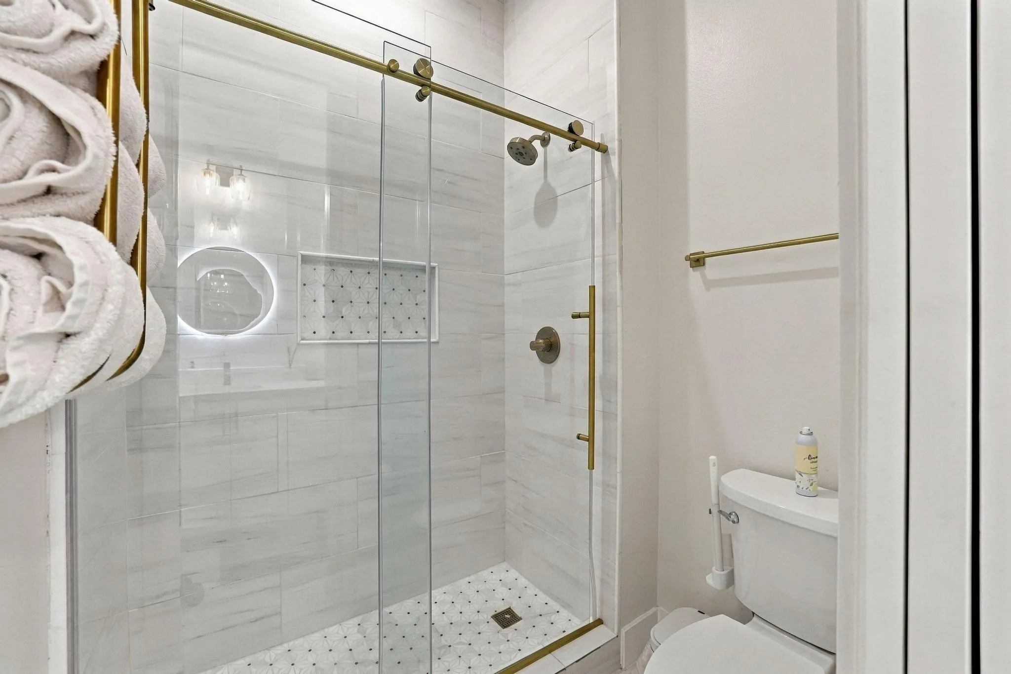 Shower enclosure featuring floor-to-ceiling light-toned tile, built-in tiled niche, brass-finish hardware, sliding glass door, and patterned tile flooring