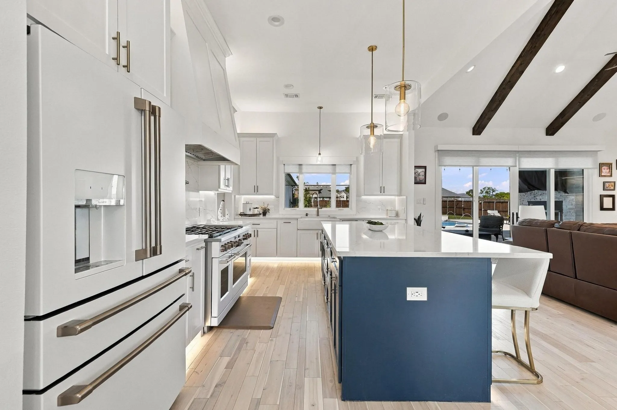 Gourmet kitchen featuring white cabinetry, a center island with a navy base, quartz countertops, wood-finish flooring, and exposed wooden ceiling beams