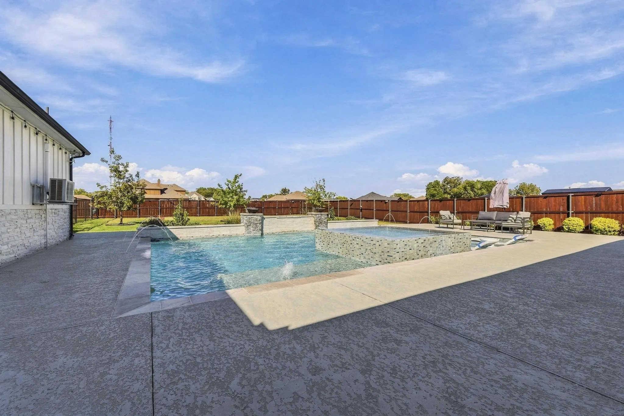 Backyard featuring an inground swimming pool with a raised spa, stone-finish water features, a stained wood privacy fence, and a stamped concrete patio
