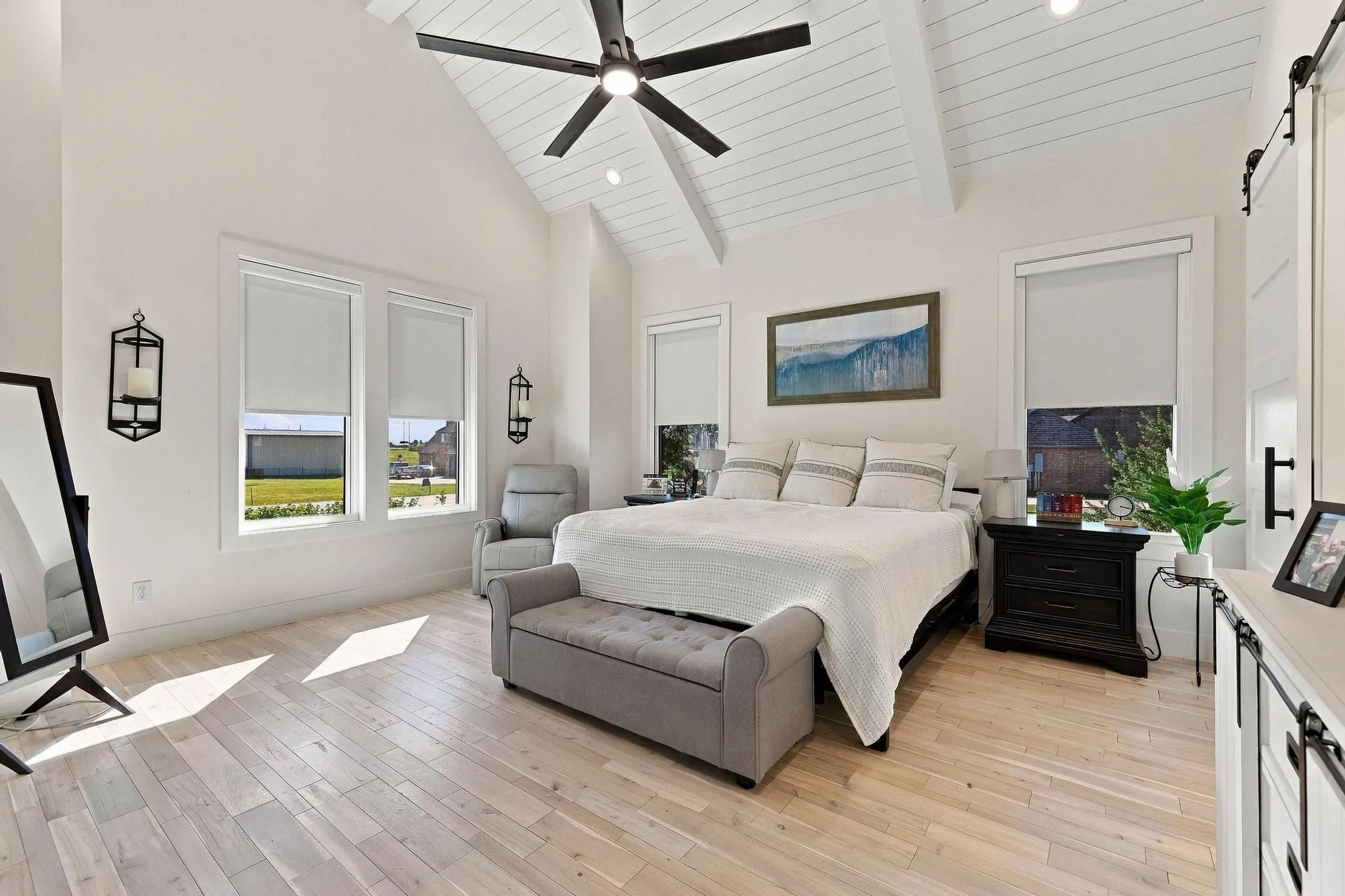 Vaulted ceiling with exposed beams, plank-style flooring, large windows, ceiling fan, and sliding barn-style door