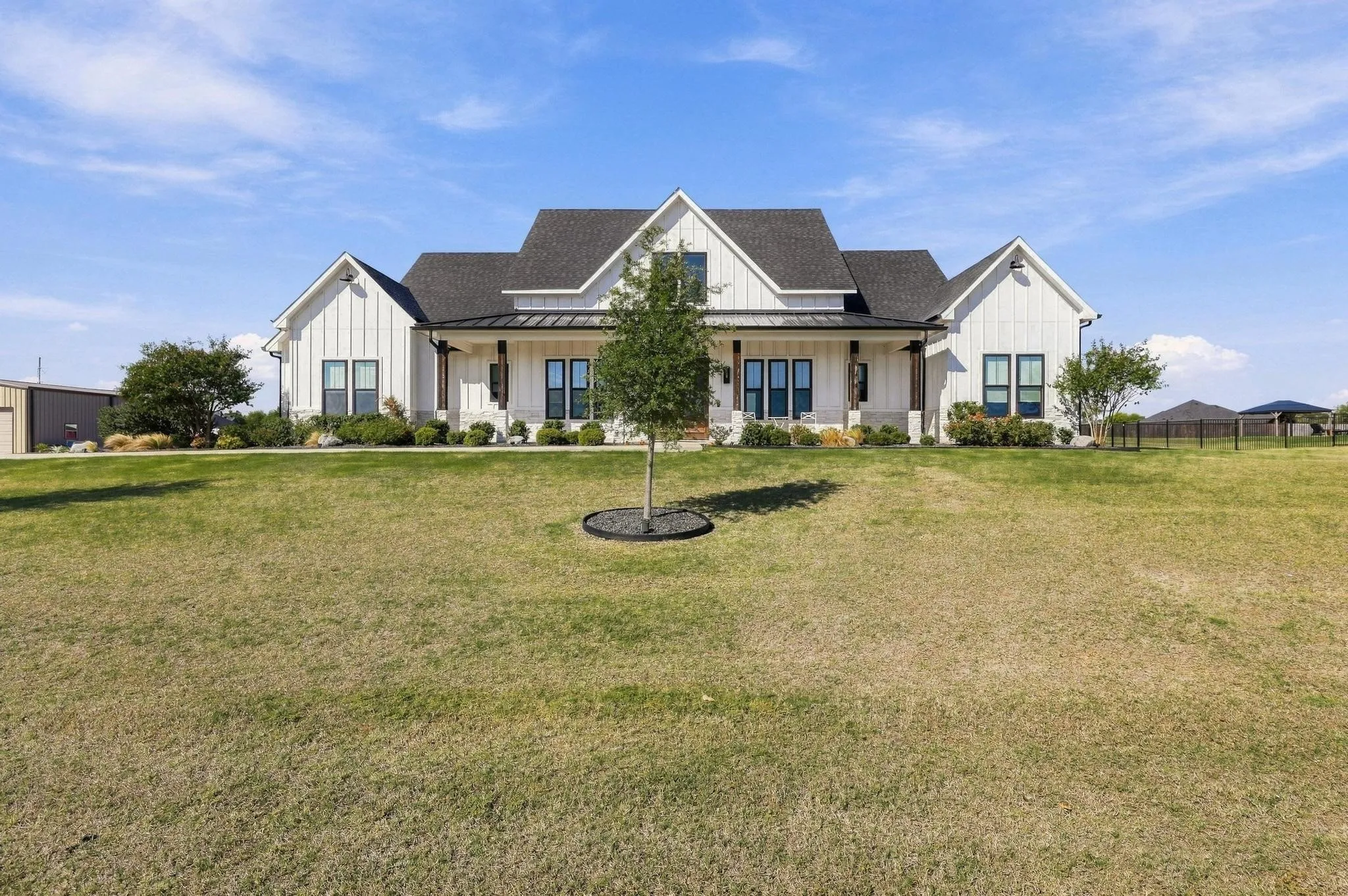 Farmhouse exterior featuring vertical siding, metal roof accents, covered porch with wood posts, and a stone base
