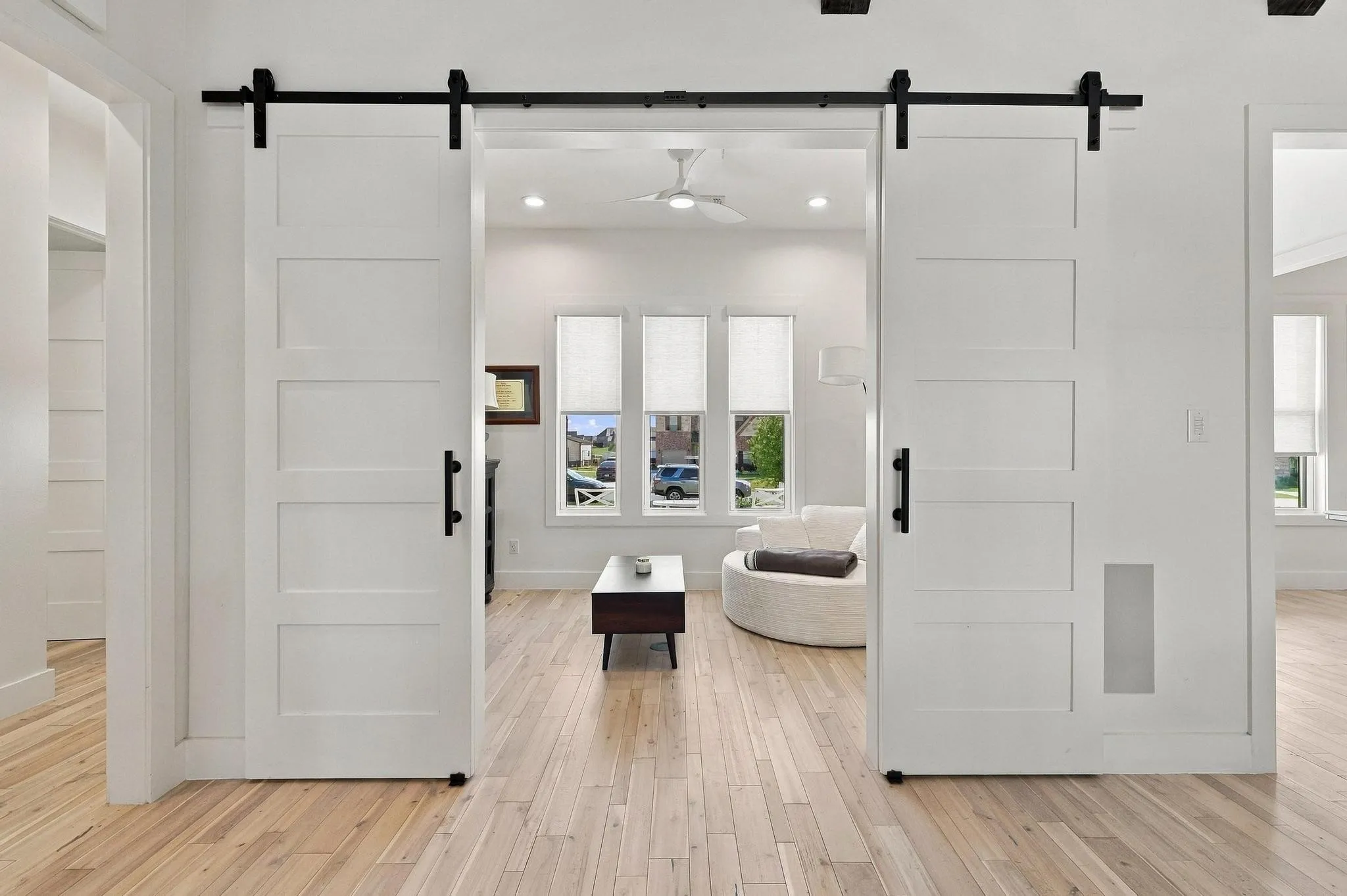 Five-panel sliding barn doors featuring matte black hardware, wood-finish flooring, and recessed ceiling lighting