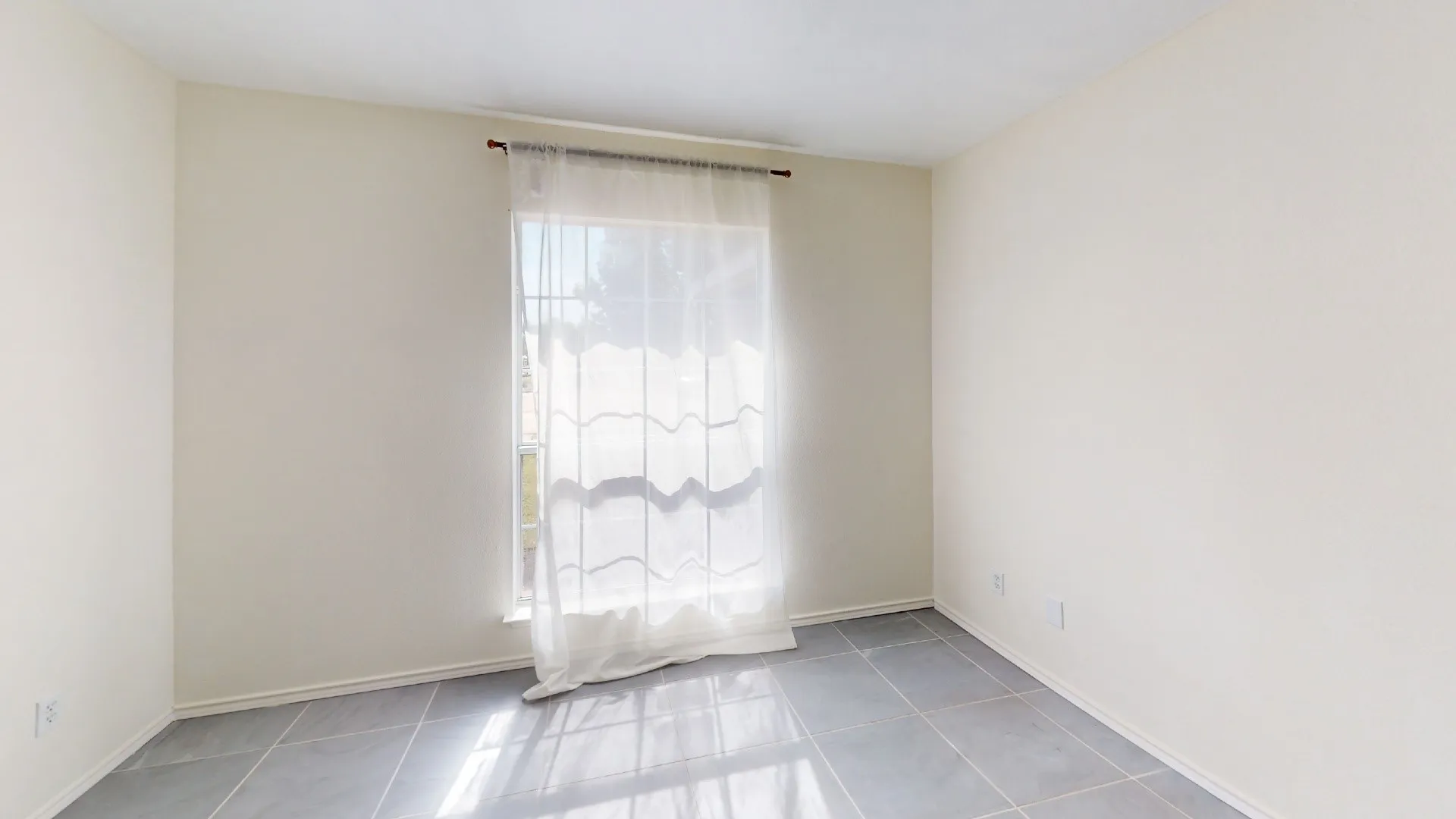 Neutral interior room featuring large-format tile flooring and a single window with a metal curtain rod