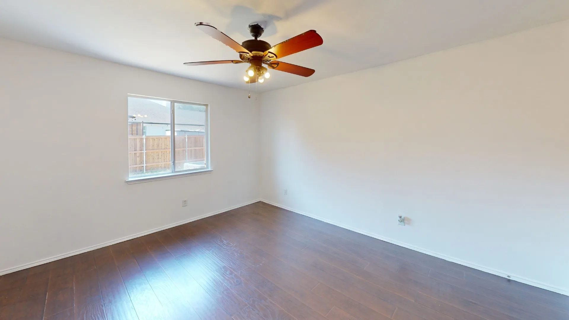 Room featuring wood-finish flooring, a ceiling fan with integrated lighting, and a window with a view of exterior fencing