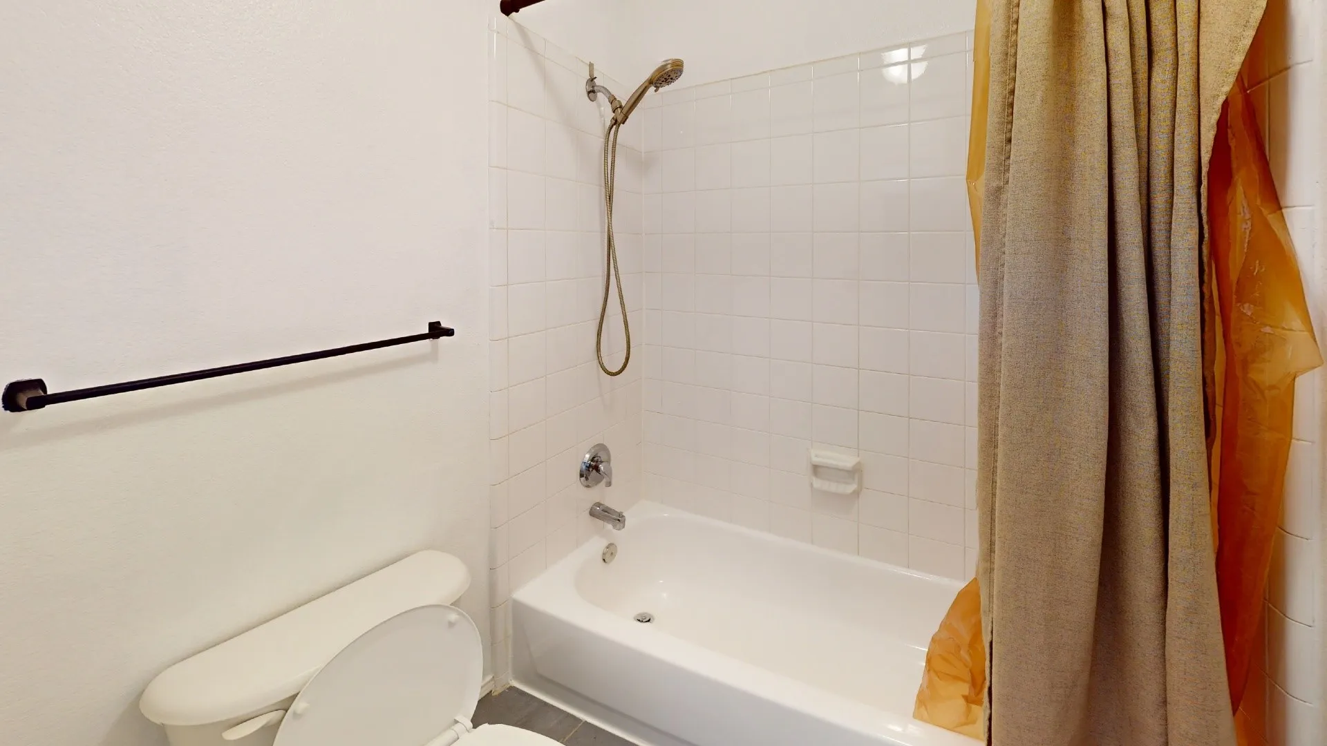Bathroom featuring a white porcelain tub, ceramic wall tile surround, adjustable handheld shower fixture, and a wall-mounted matte black towel bar